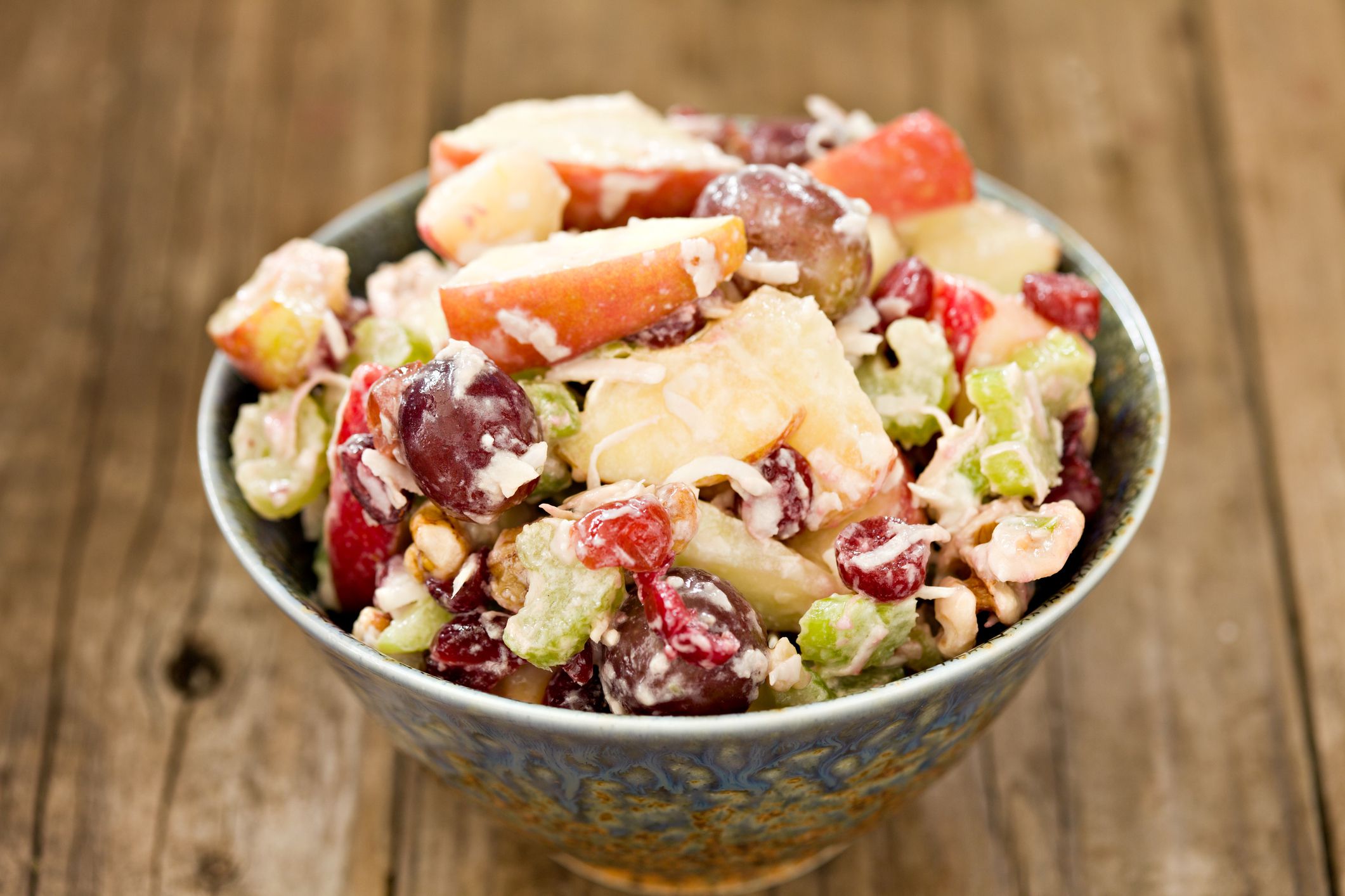 A high angle close up of a fancy blue ceramic bowl full of freshly made Waldorf Salad. Shot on a grungy old wooden table.