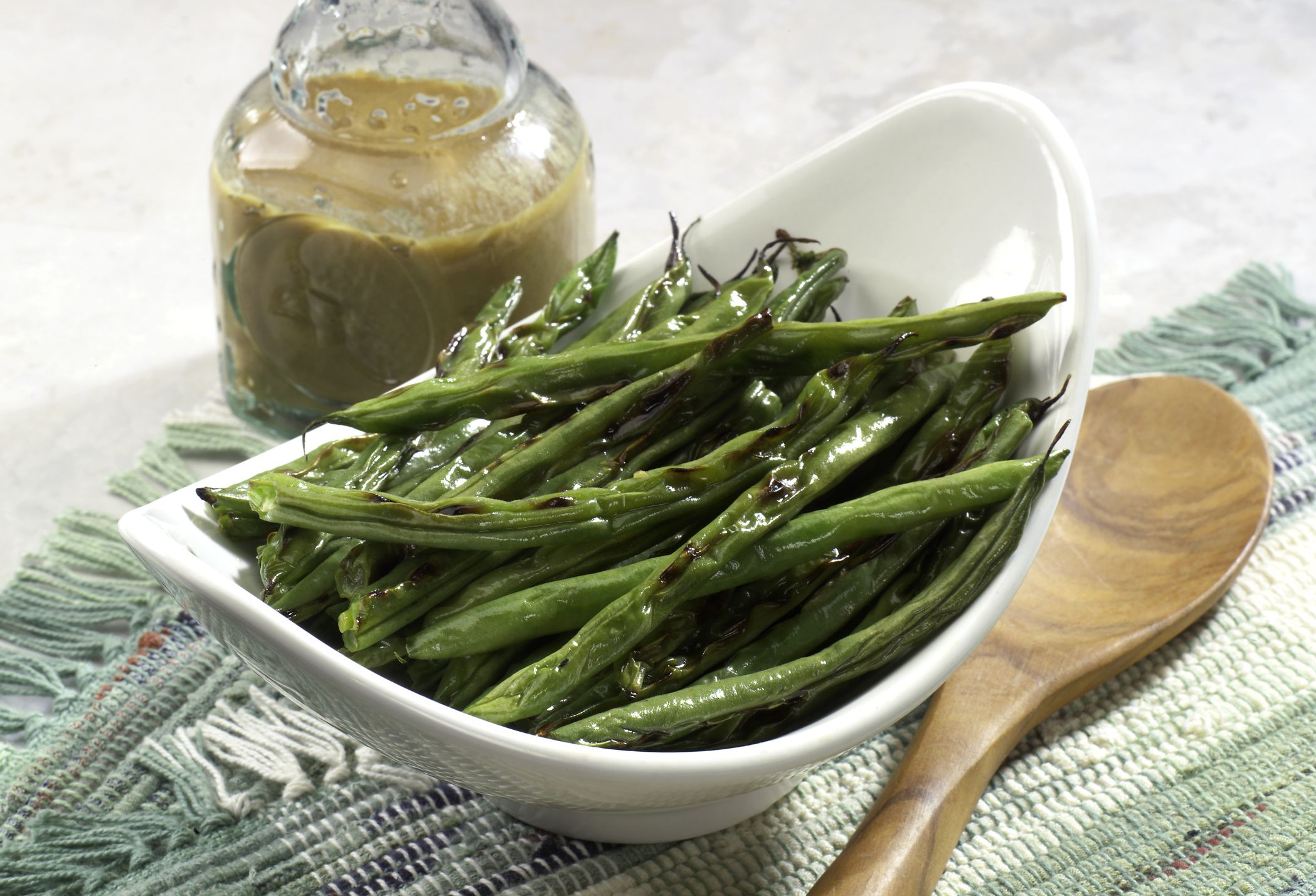 Side dish of grilled string beans on table setting. Vinaigrette dressing and wooden spoon