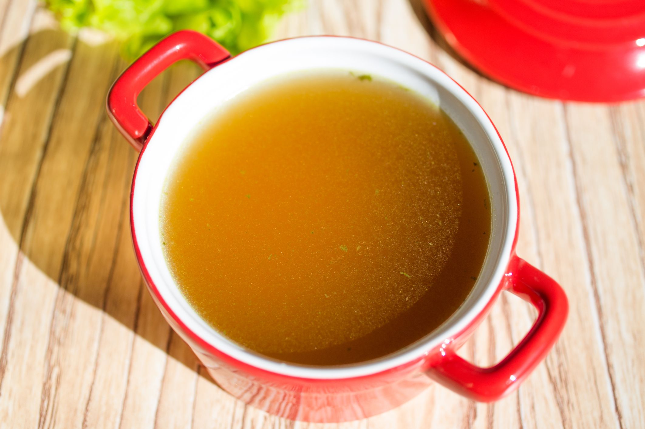 Chicken broth, bouillon, clear soup in a cup next to fresh herbs.