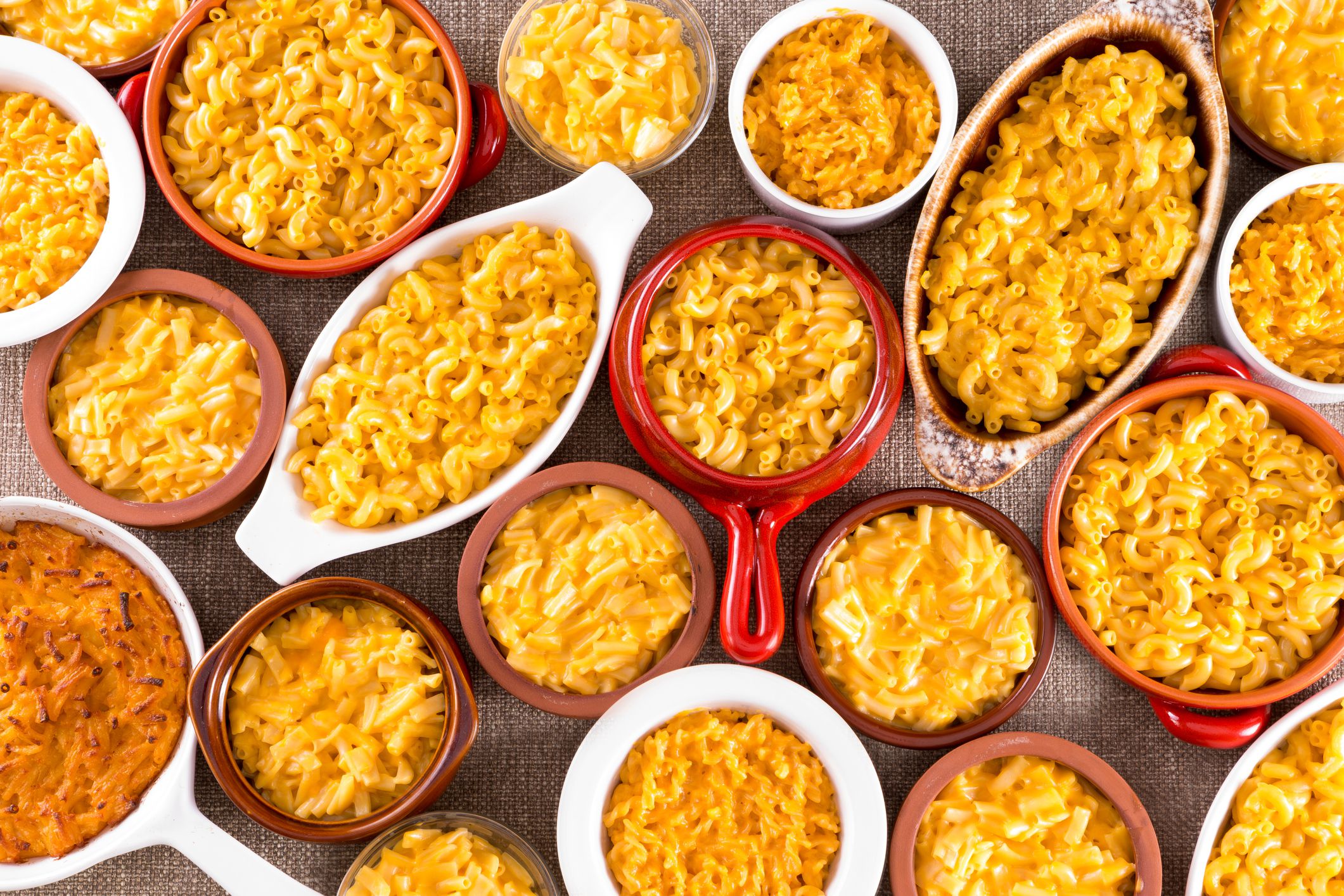 Several bowls filled with different types of cheese macaroni served on cotton table cloth