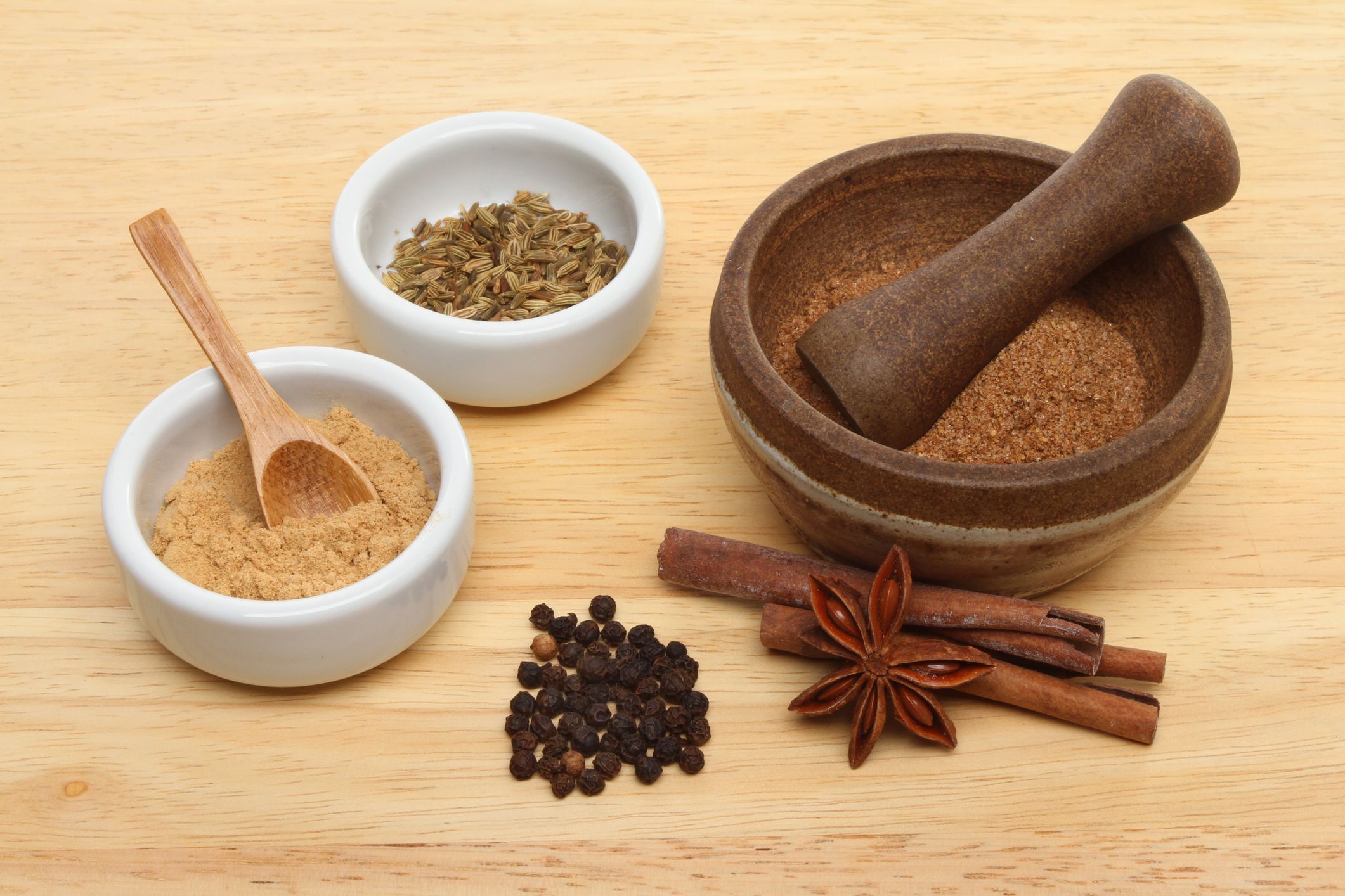 Ingredients for Chinese five spice with ramekins and a pestle and mortar on a wooden board