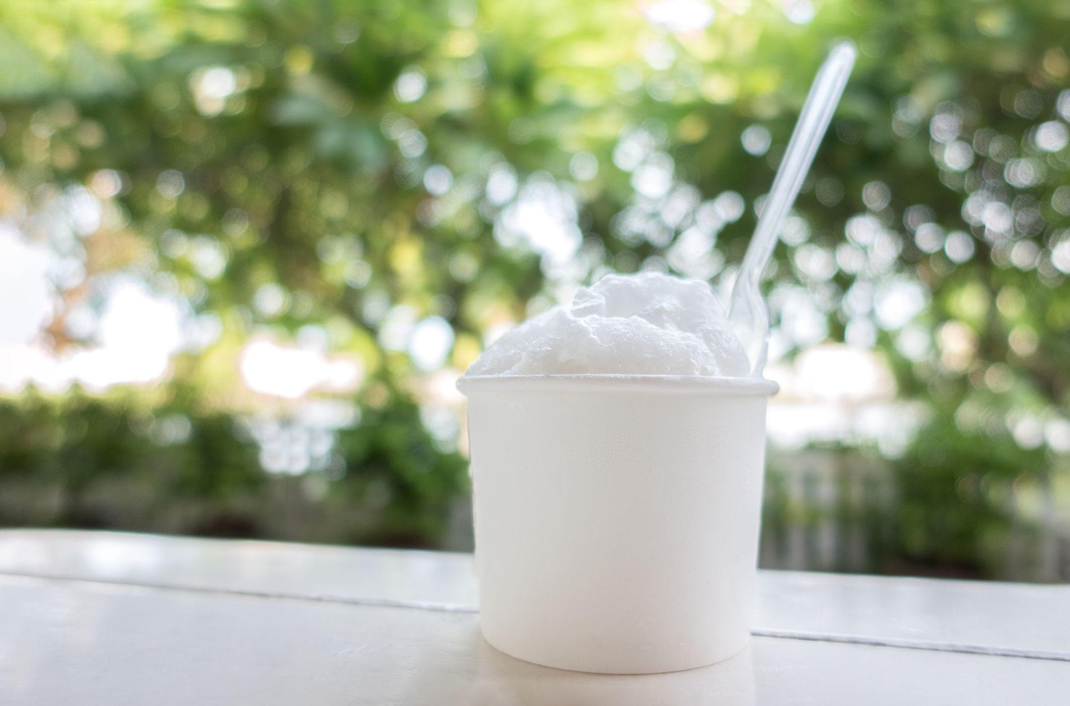 white coconut ice cream in white cardboard paper tub cup with plastic spoon on white wooden table