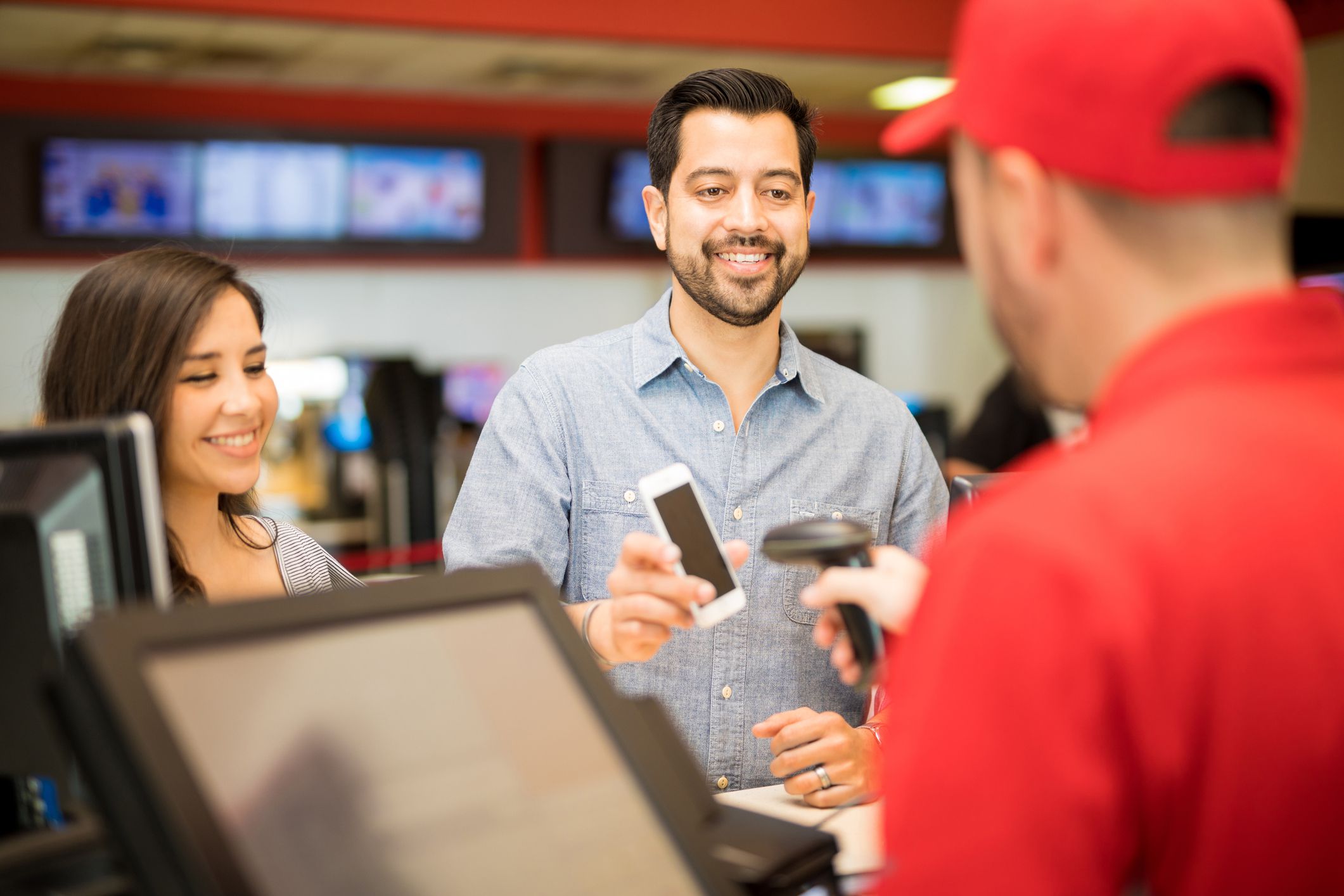 Attractive couple buying tickets at the movie theater and using a smartphone to show a barcode to an employee