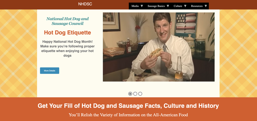 A man in a suit smiles at the camera while holding a hot dog at a dining table. The webpage promotes hot dog etiquette for National Hot Dog Month, with orange and yellow themed design elements.