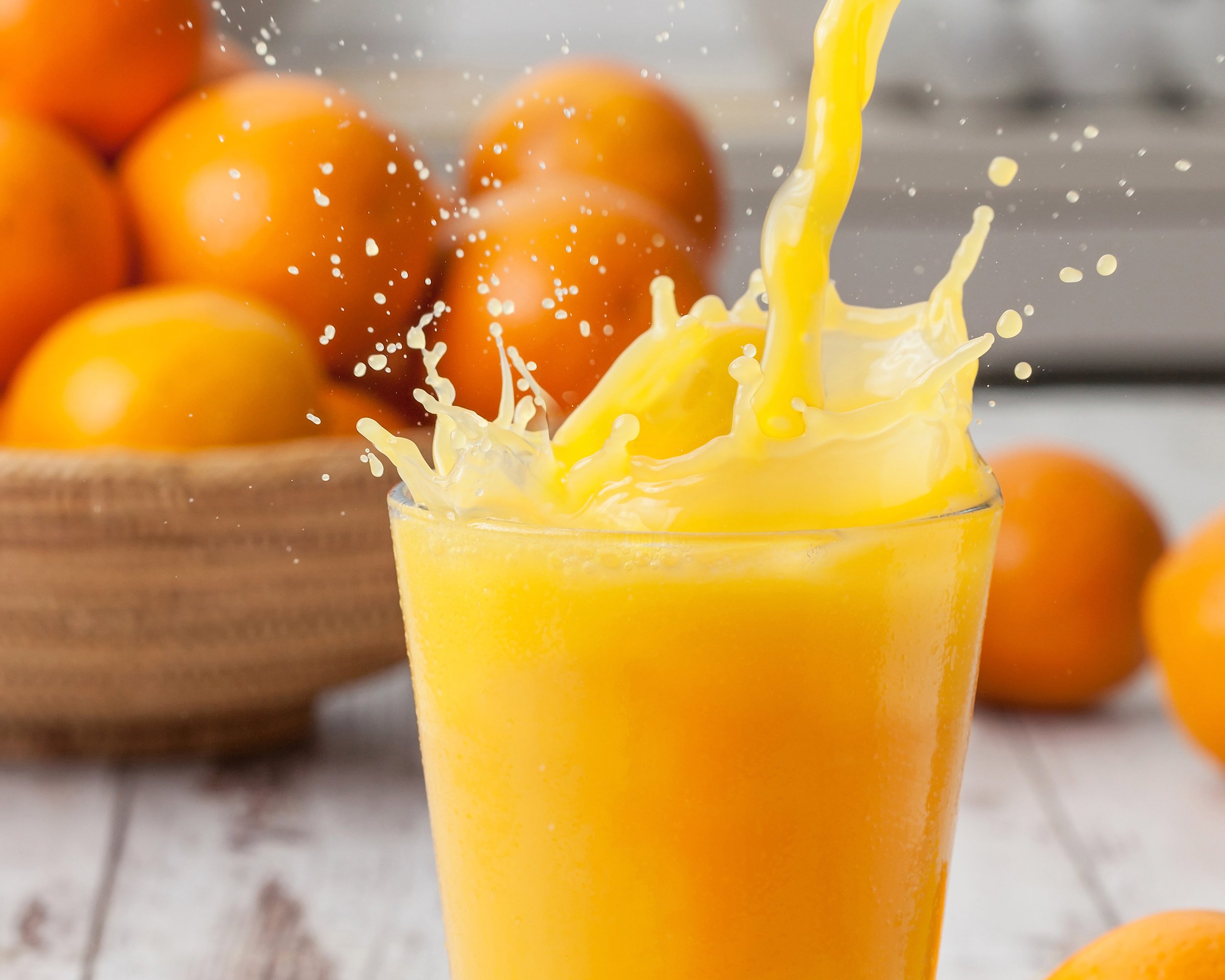 orange juice with splash and oranges in background