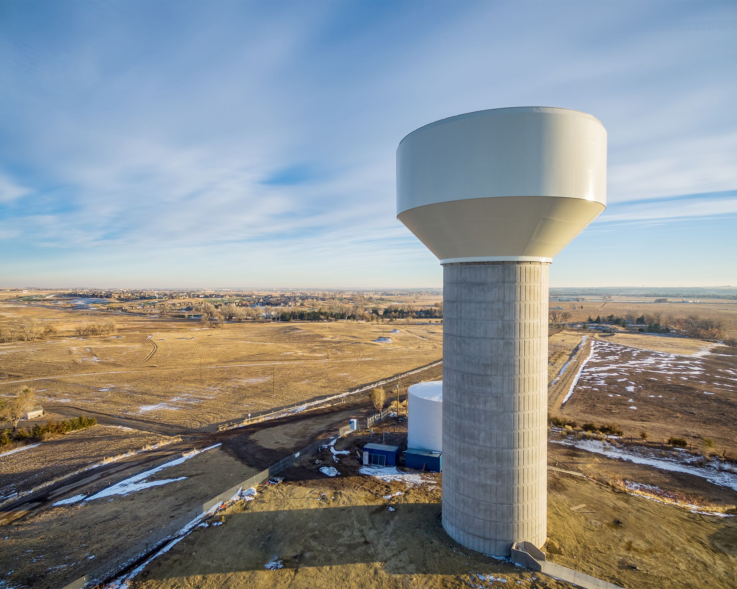 Aerial view of a water tower along the Colorado Front Range during winter with some snow on the ground with a new house development in the background on a sunny day