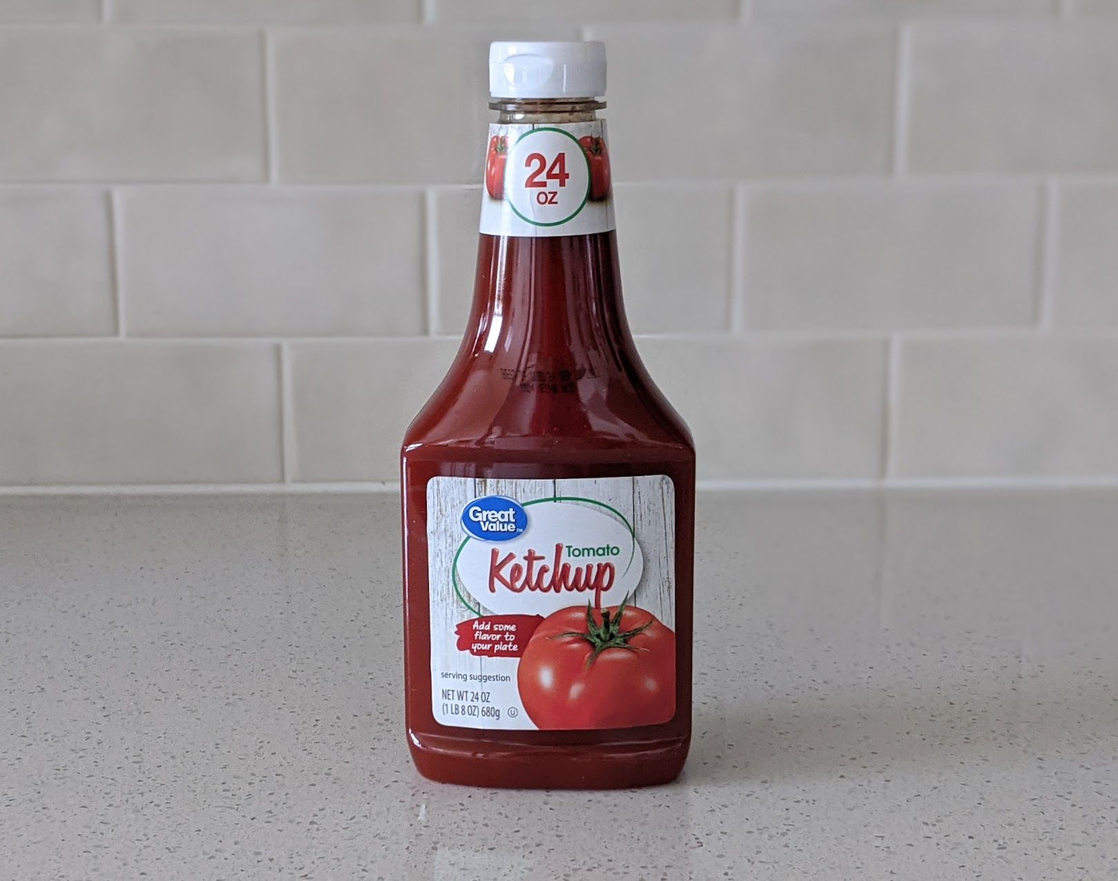 A bottle of Great Value Tomato Ketchup on a speckled ivory kitchen countertop, light beige tile wall in the background