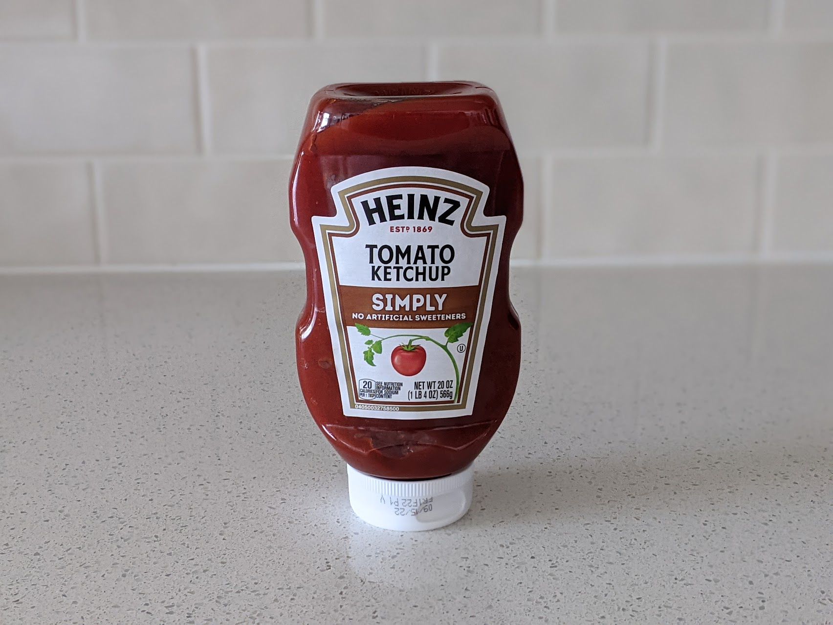 A bottle of Heinz Simply Tomato Ketchup on a speckled ivory kitchen countertop, light beige tile wall in the background