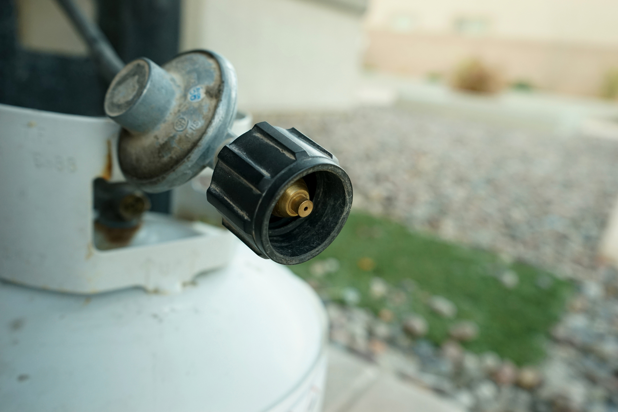 Closeup of a black nozzle on a white propane tank, selective focus, top of tank, blurred background of outdoor yard of a home