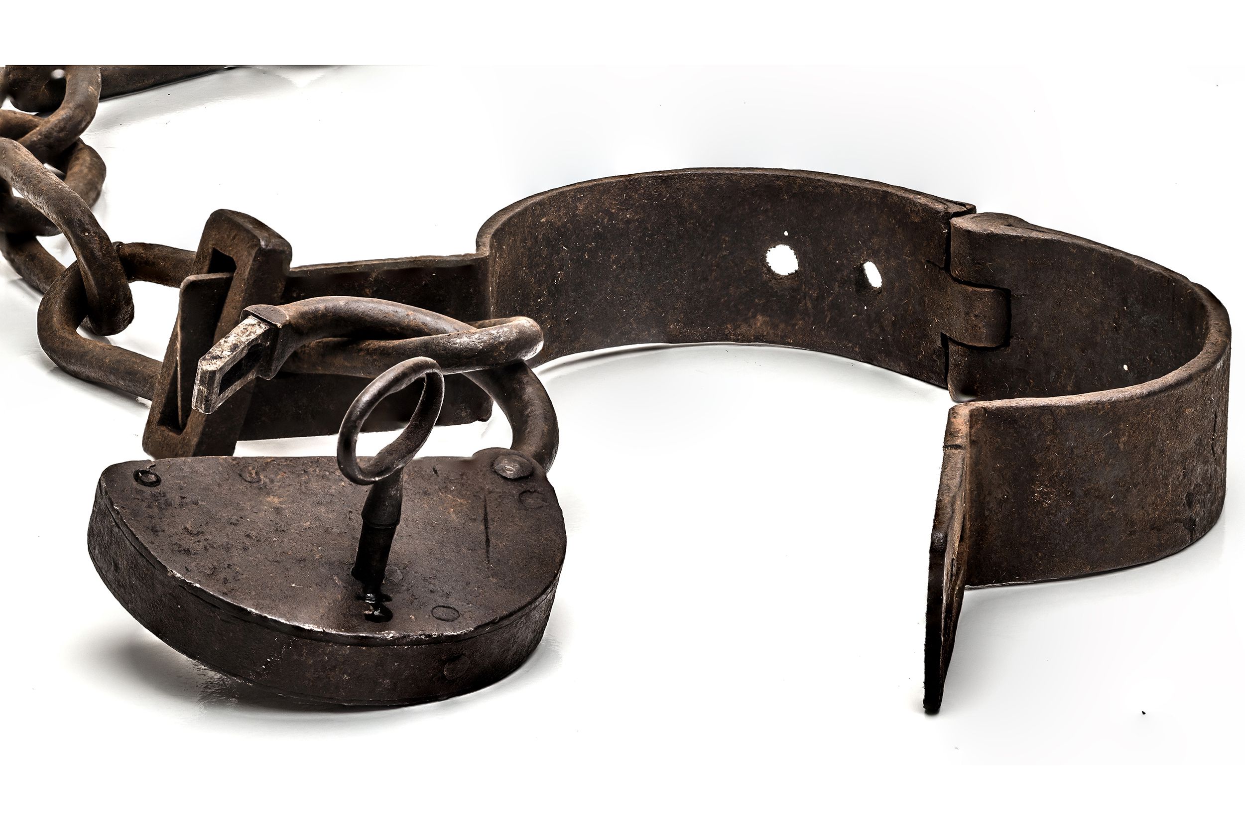 Closeup of rusty old shackles with a padlock, a key, and an open handcuff, against a white background with the chain in the top left