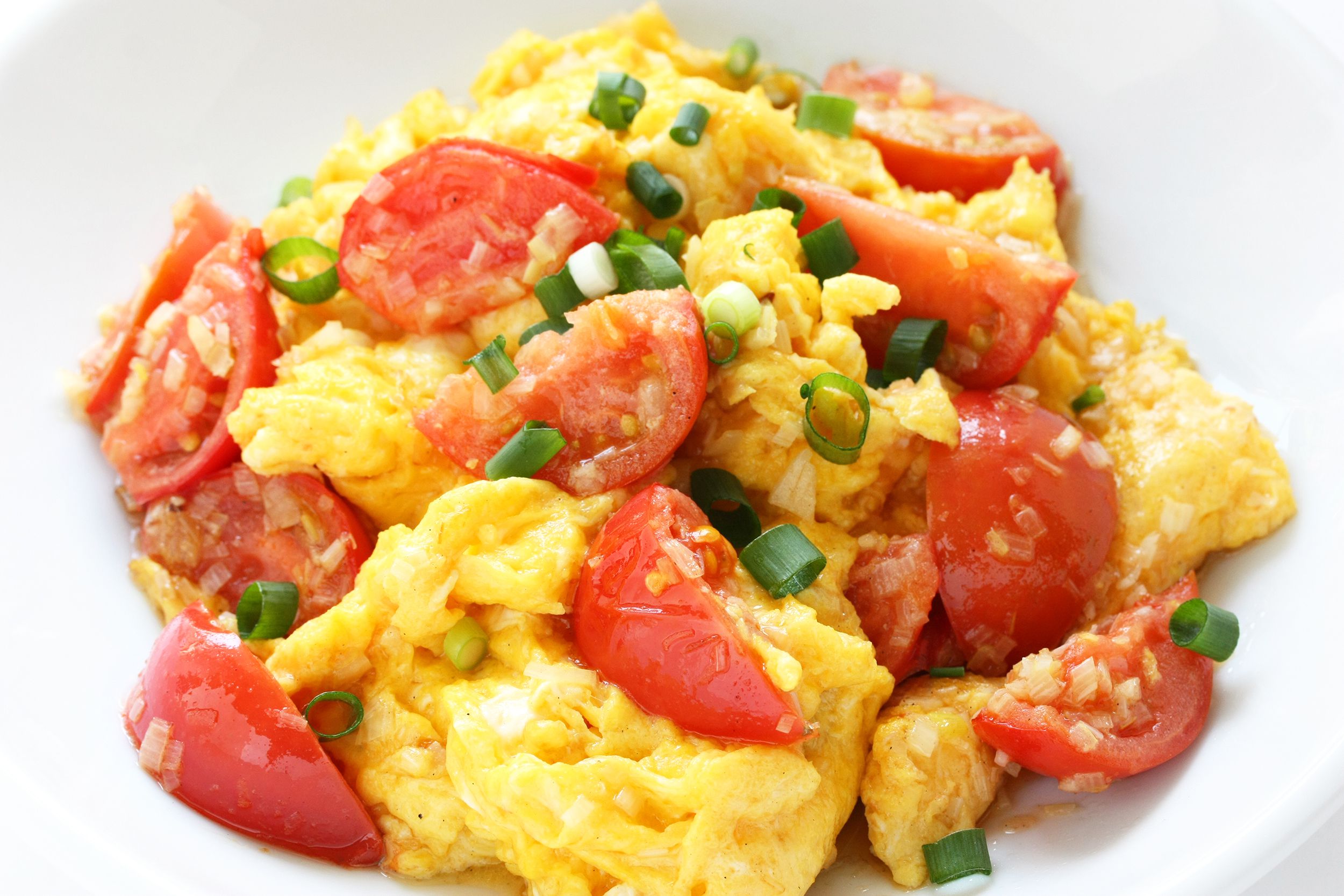 Closeup of scrambled eggs with tomatoes in a white bowl