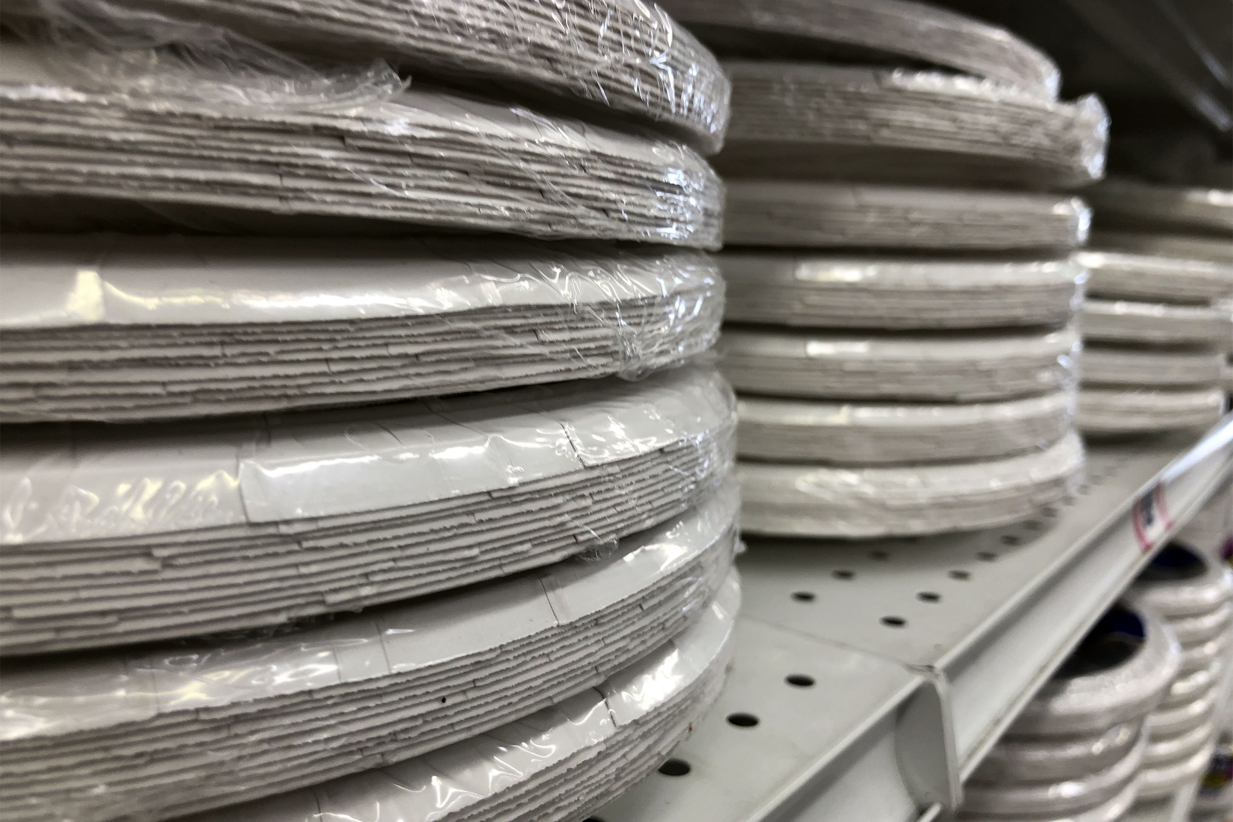 Closeup of several packages of paper plates on a shelf at store, selective focus on the left stack, blurred rest of shelf and shelf below