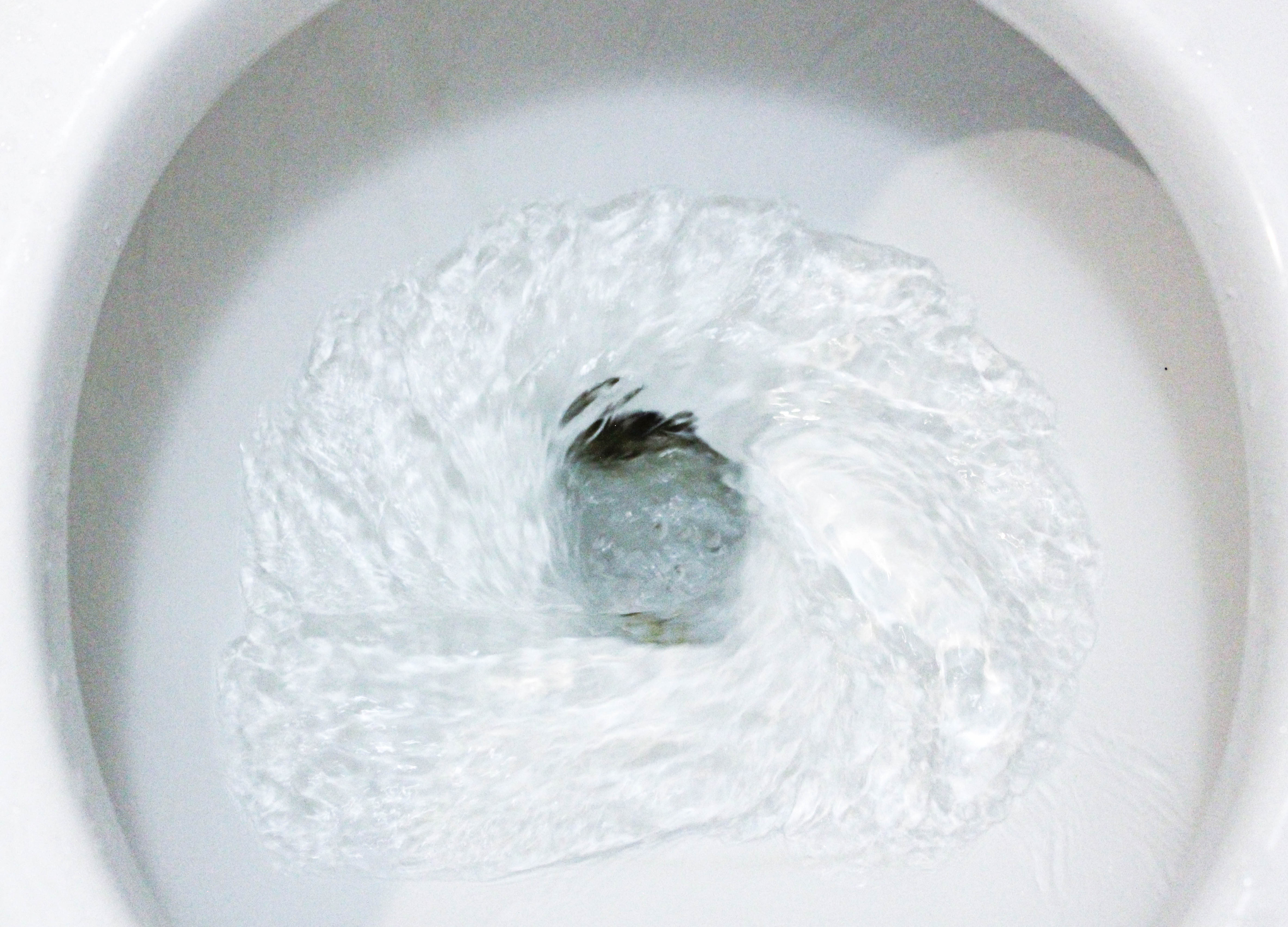 Closeup of water being flushed down the toilet, white toilet bowl and seat around the edges