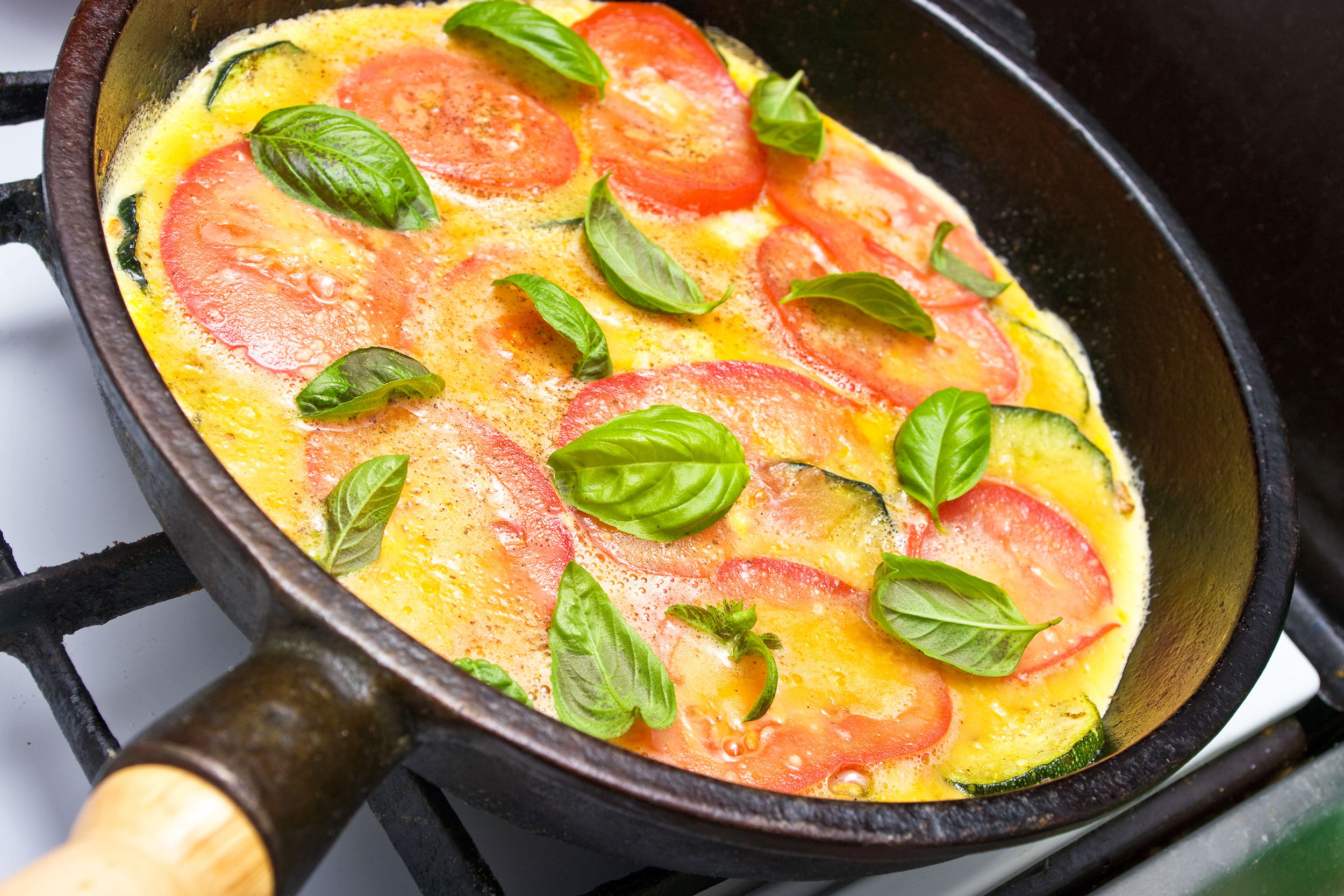 Focus on tomato and herb omelet in a cast iron skillet on a black burner of a stove with a blurred background