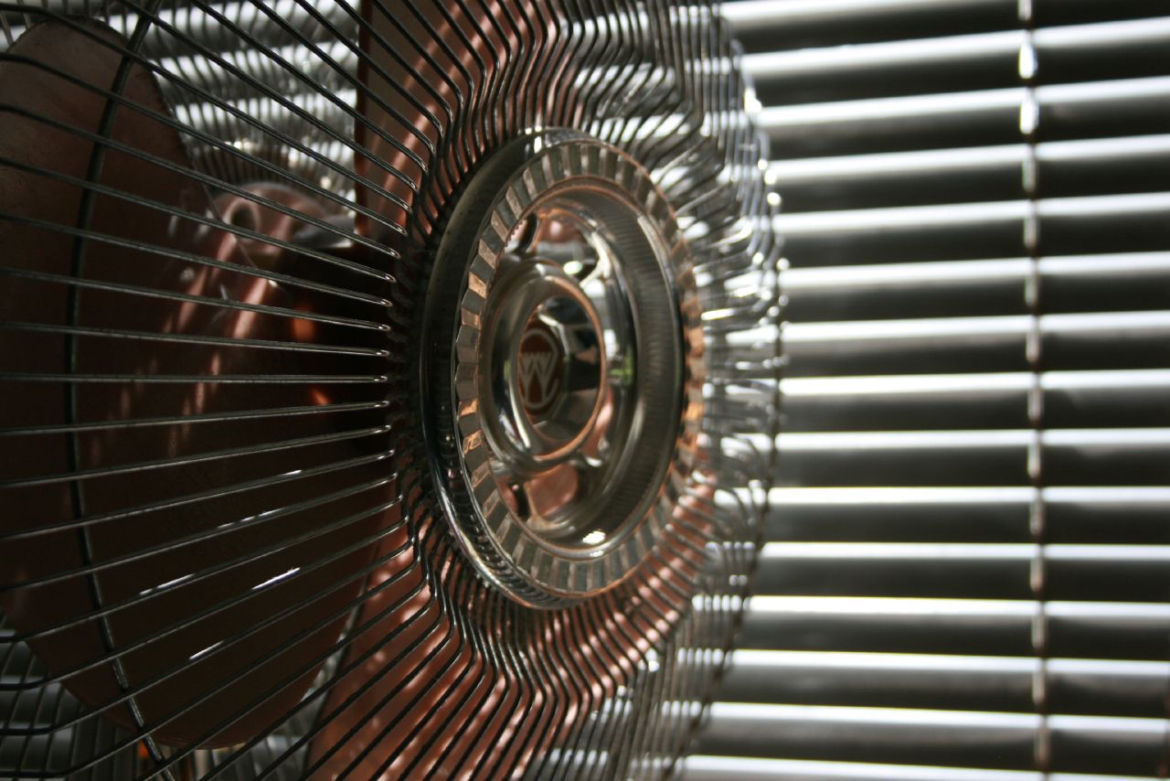 Focus on wired bladed fan, selective focus, sunlight coming through dark grey window blades in the background