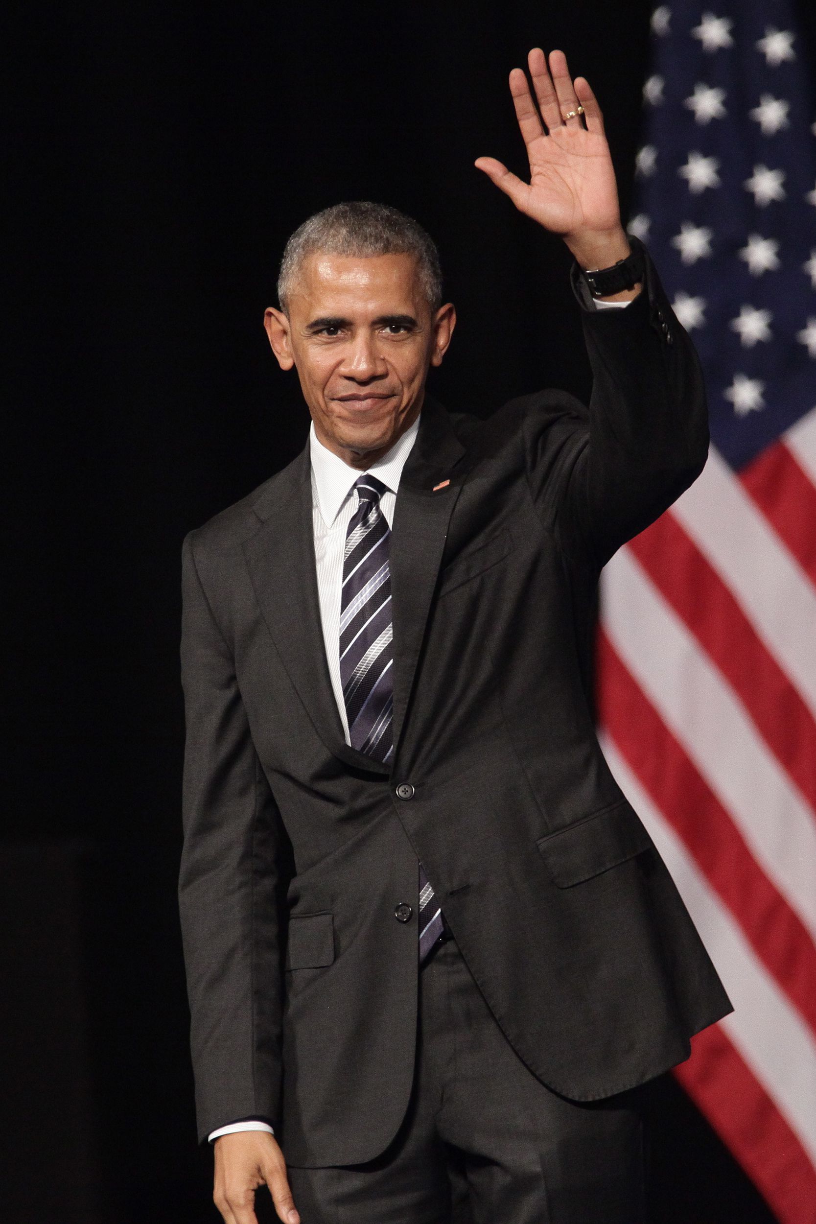 Former President Barack Obama waves to the crowd before he delivers a speech at the new opera of Athens, Greece with both the U.S. flag and Greece flags blurred in the background