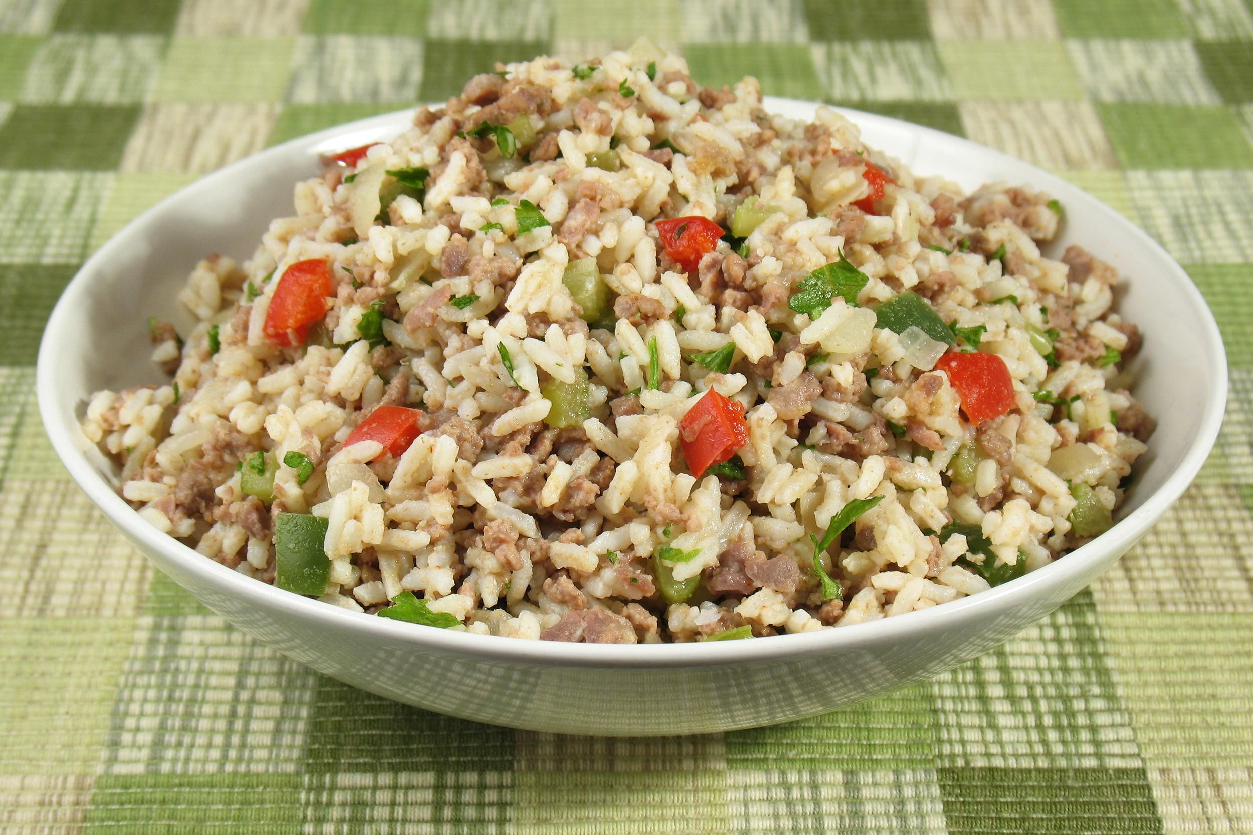 One pot New Orleans dirty rice in a white porcelain bowl on a white, sage green, and avocado green checkered tablecloth