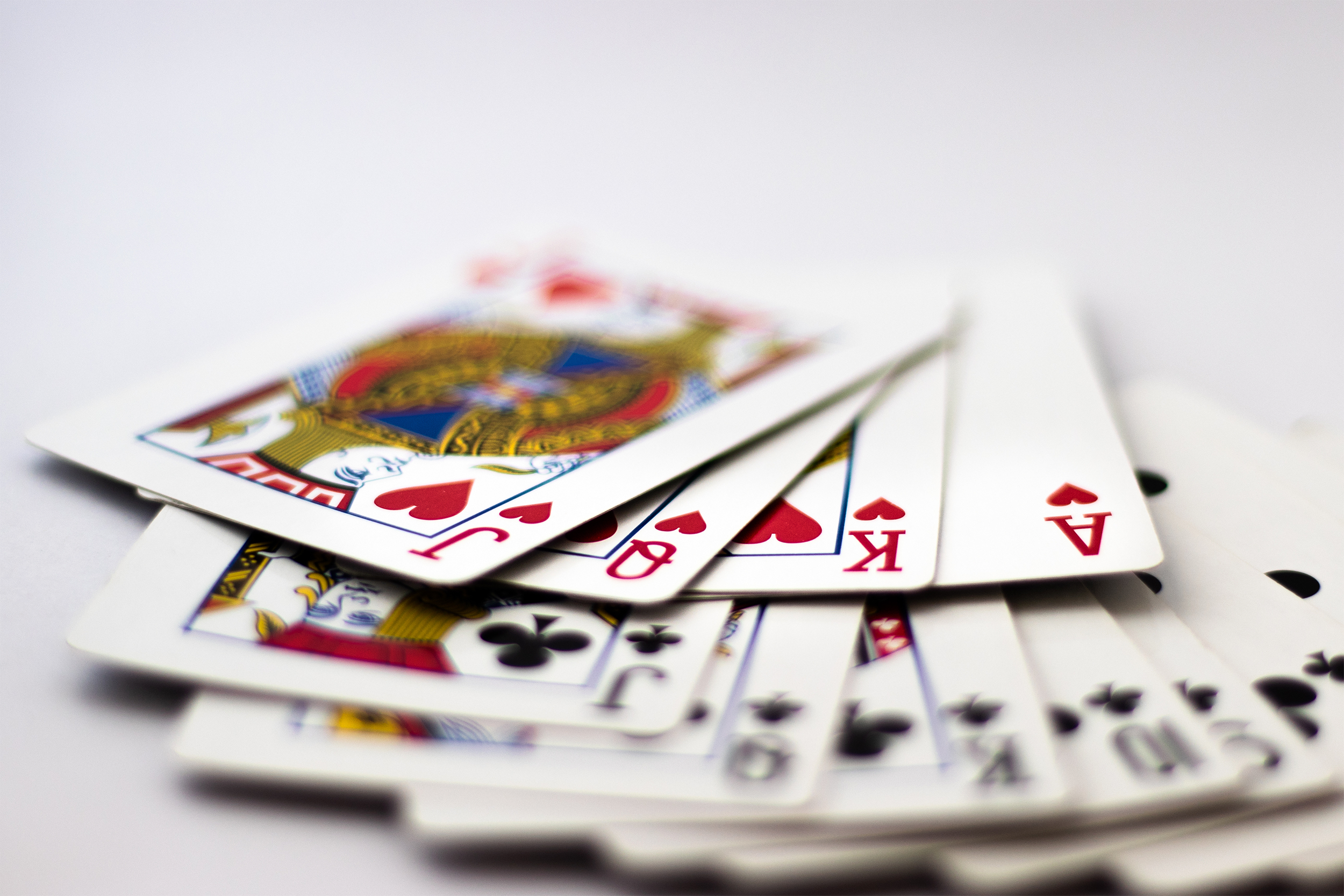 Playing cards, selective focus on four, rest blurred, displayed in a few rows of fans, on a light grey background
