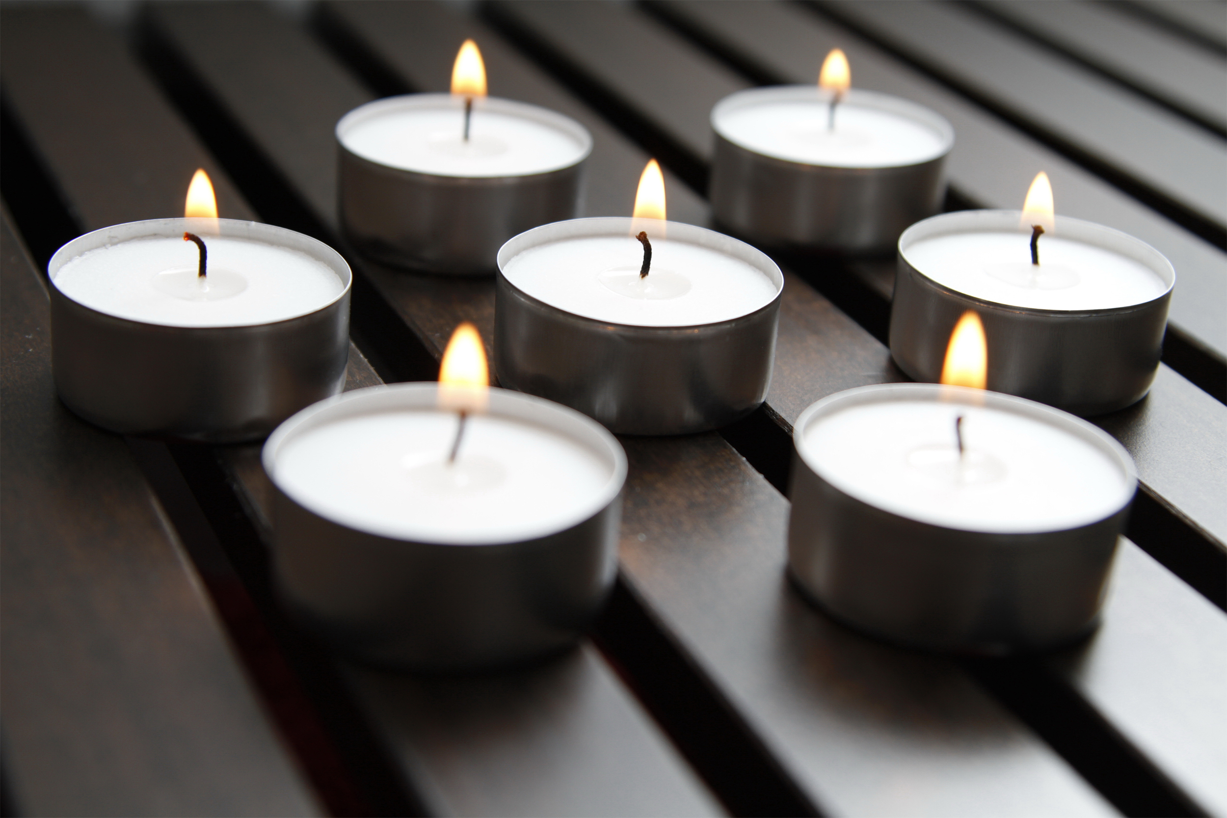 Seven lit tea lights, selective focus, arranged in a rectangle on a dark brown wooden fenced table, slightly blurred