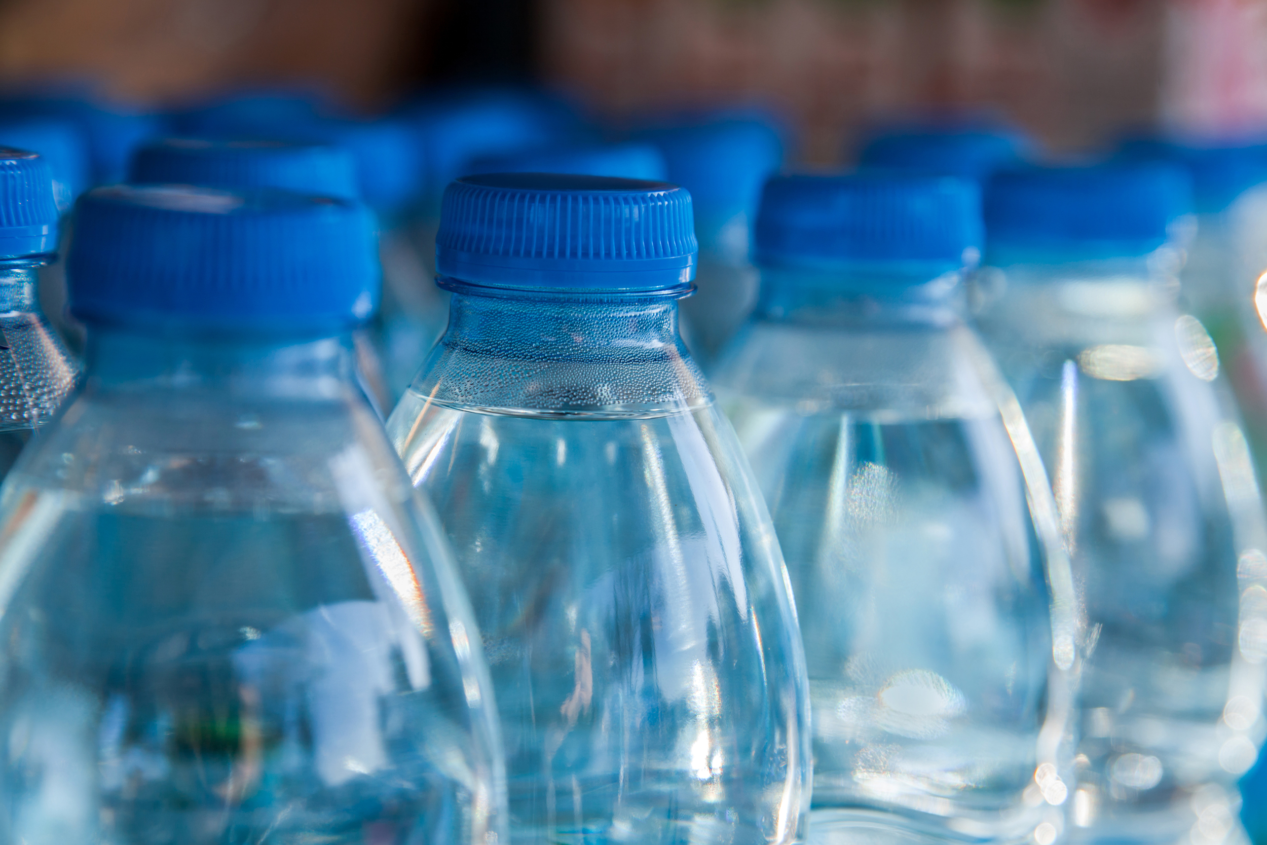 Several plastic water bottles with blue caps, selective focus, half view, blurred background of wood