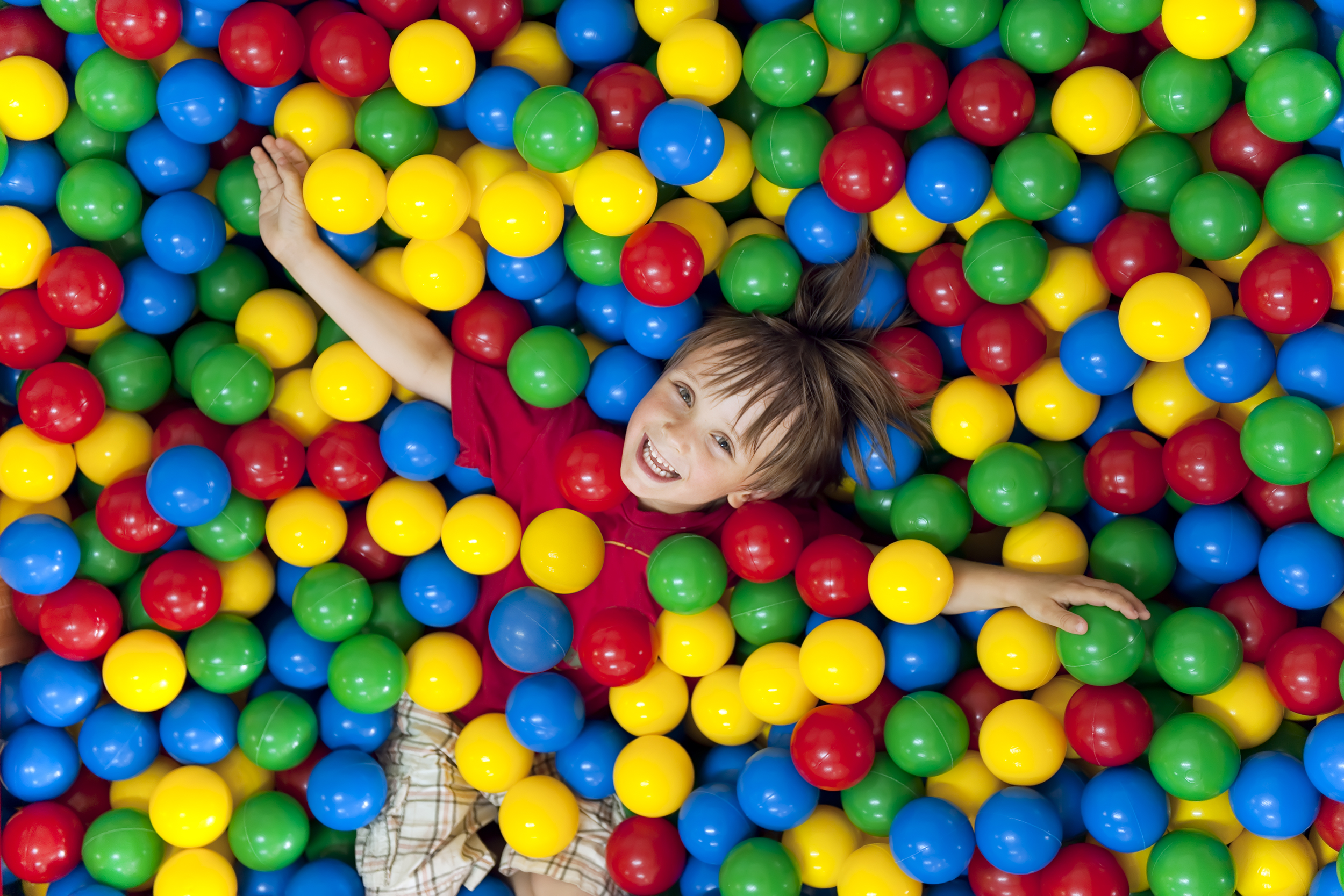 Smiling child looking up from a ball pit with colorful plastic balls