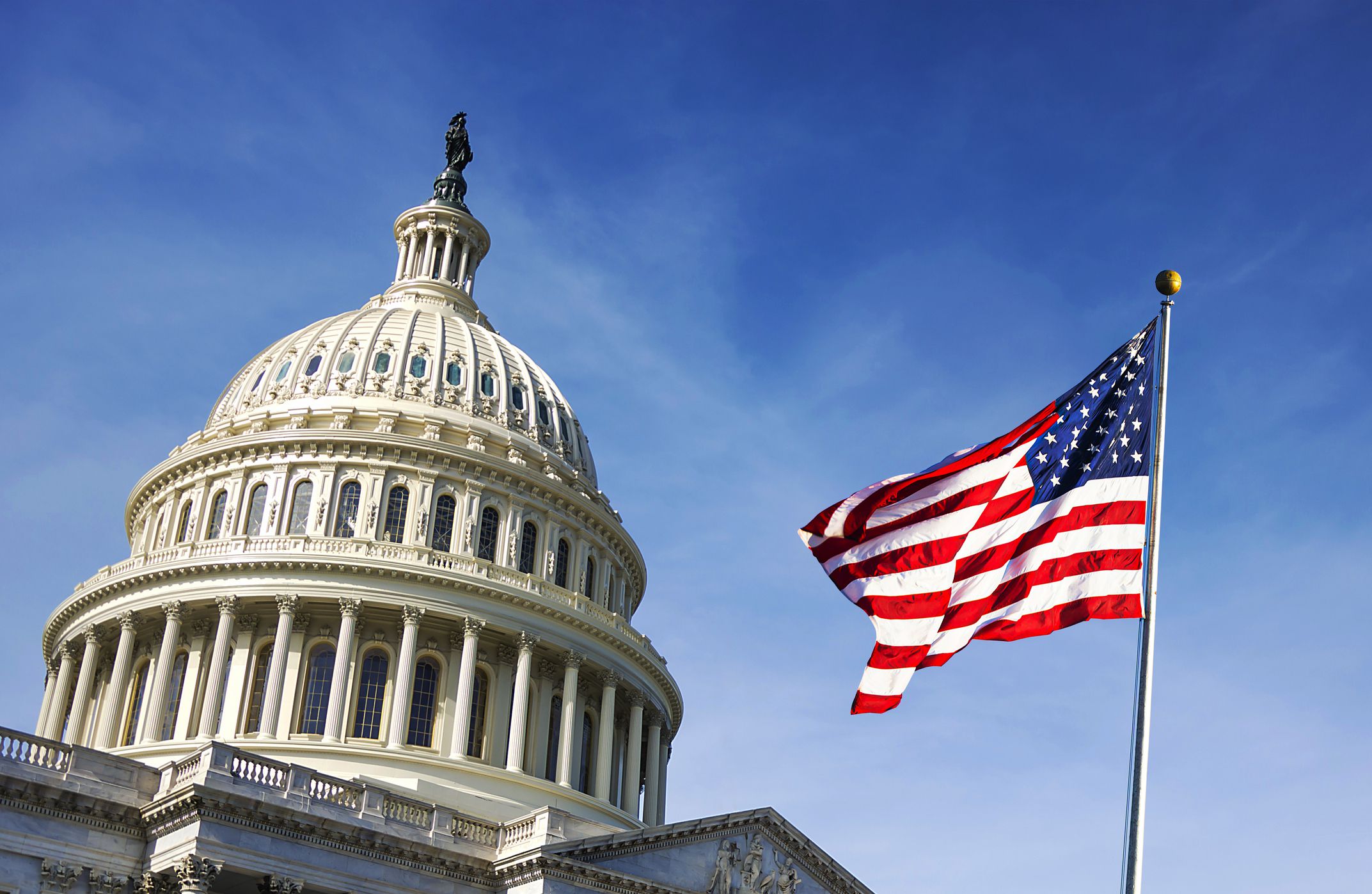 Waving U.S. flag to the right with the U.S. Capitol dome in the background to the left, Washington, D.C., against a clear and vivid blue sky