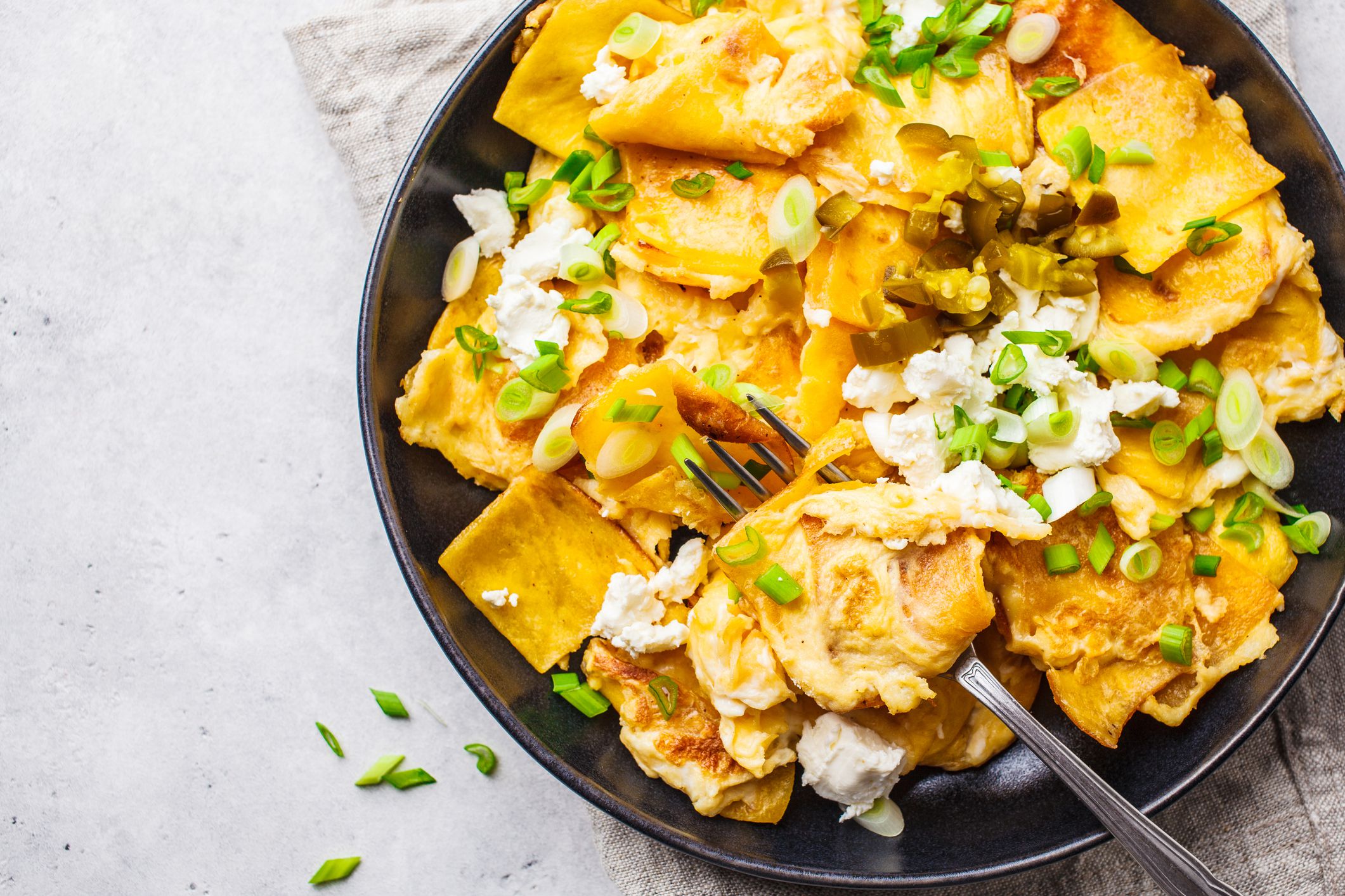 Mexican tortilla egg migas with feta and green onions in a black plate on a white background, top view. Mexican food concept.