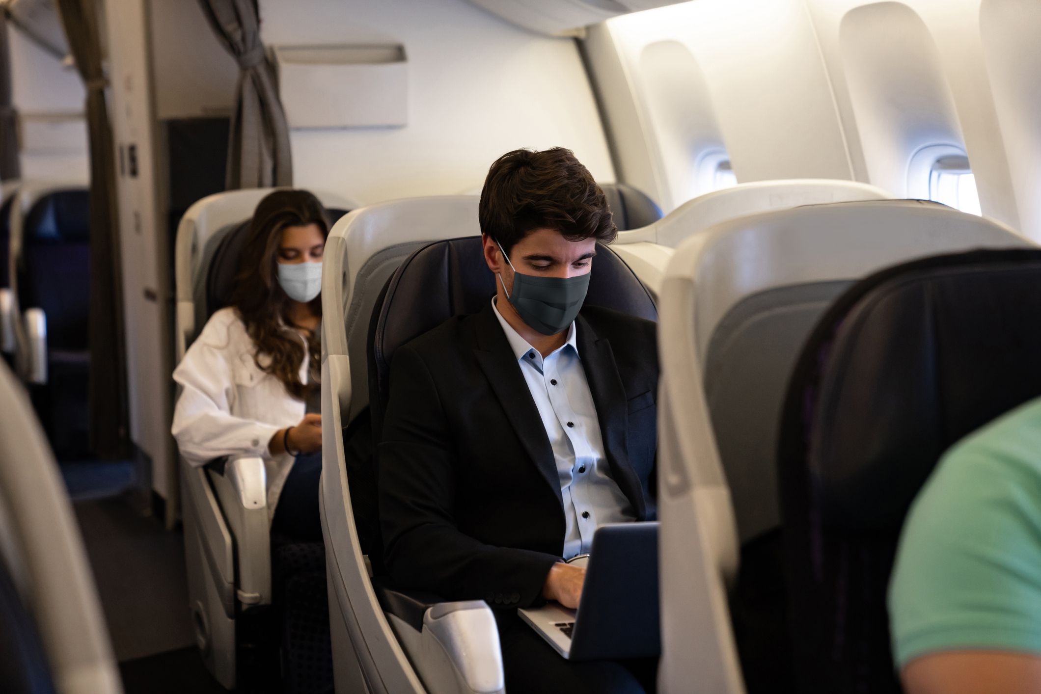 Business man traveling and wearing a facemask on the plane while using his laptopâ COVID-19 pandemic lifestyle concepts