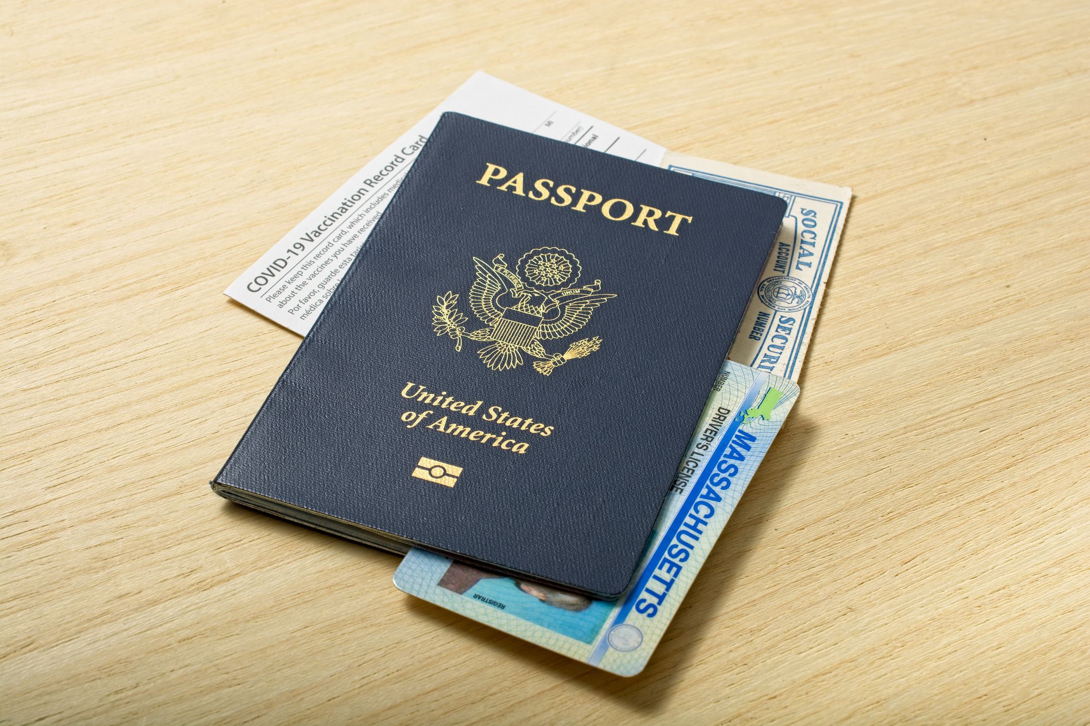 Contemporary Personal Identification Information set of passport Social Security Real ID and COVID-19 Vaccination card all lying on wooden tabletop.
