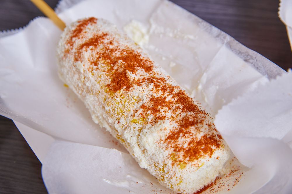 Elotes elote corn street food Mexican food dish cotija cheese spicy chili powder on white dish