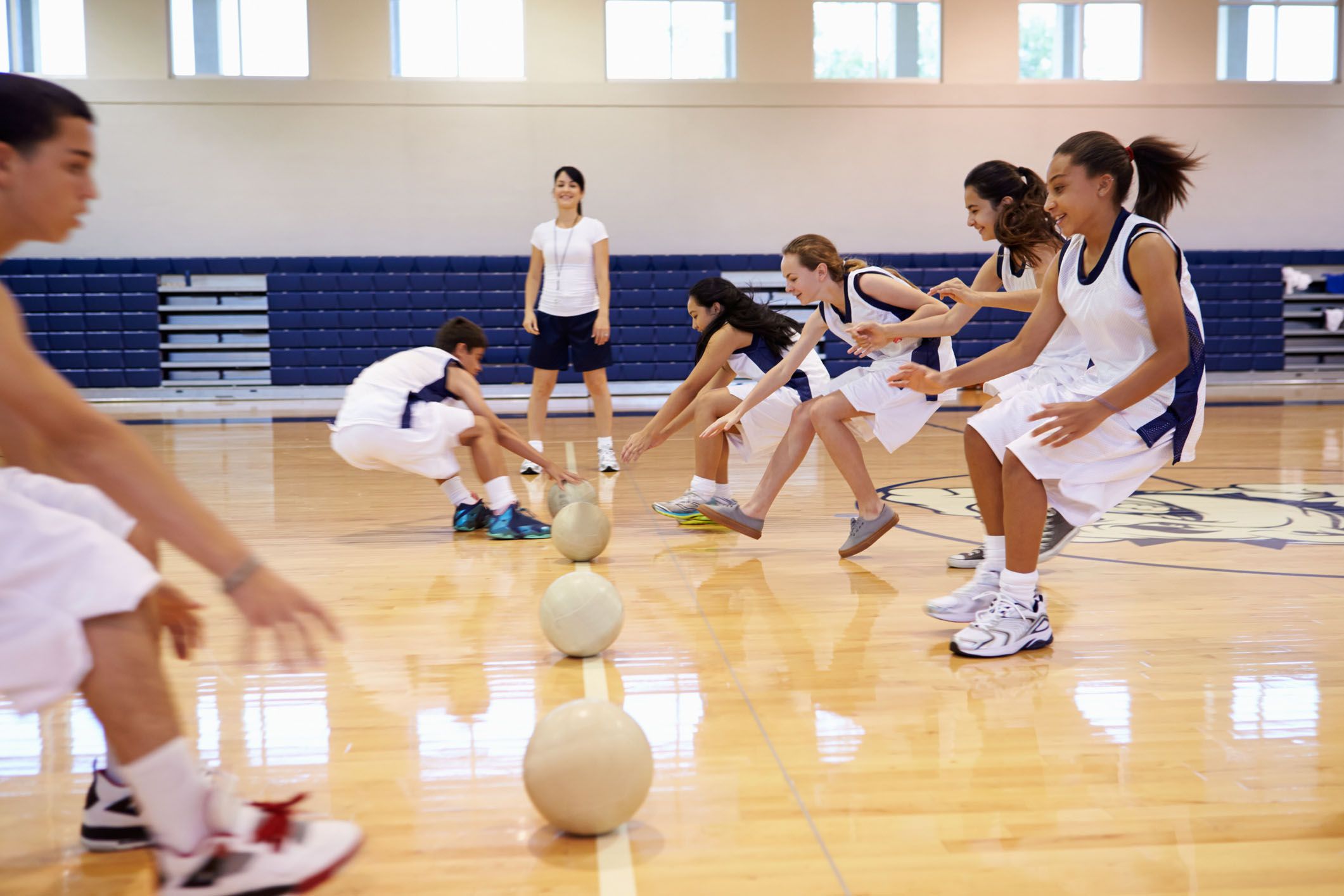 students playing dodgeball in gym as coach watches