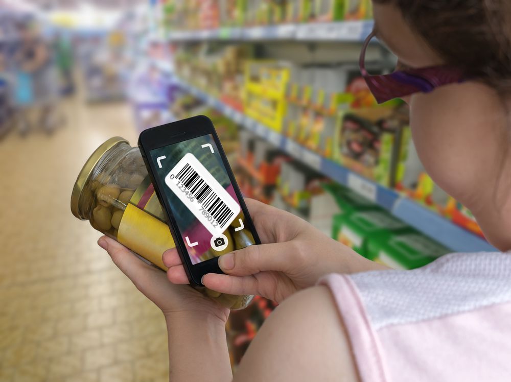 Woman is shopping in supermarket and scanning barcode with smartphone.