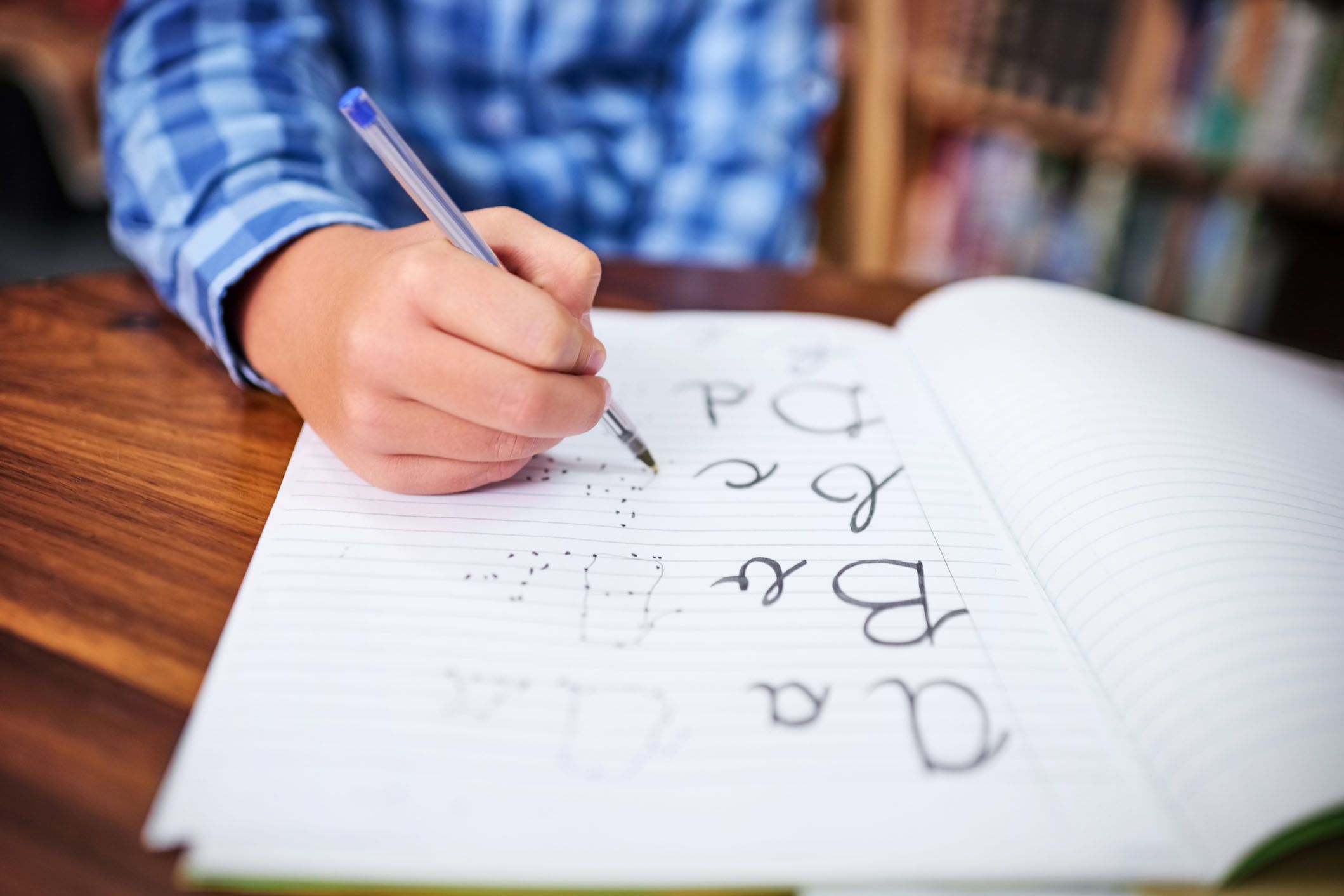 student practices tracing cursive letters in notebook in library