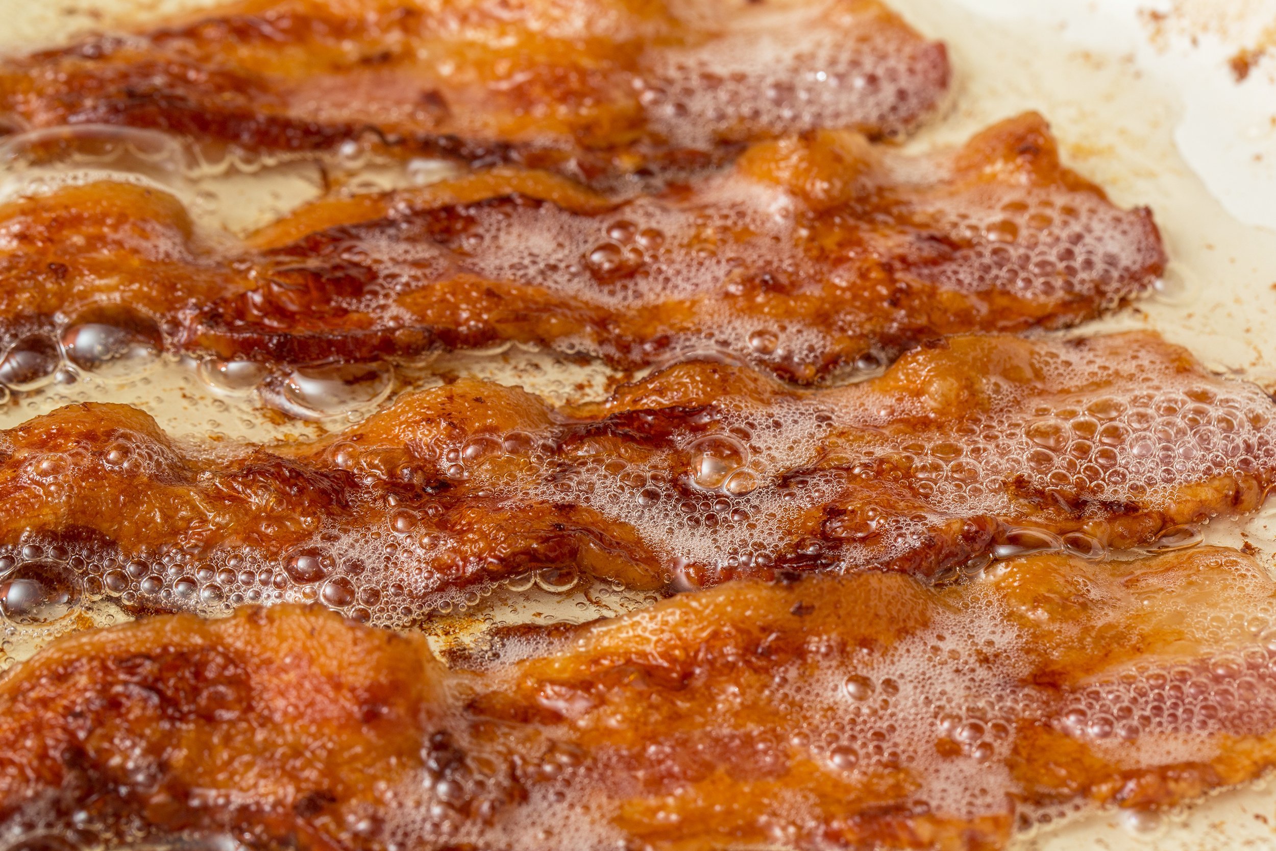 bacon cooked cooking in white pan skillet on flat top stove