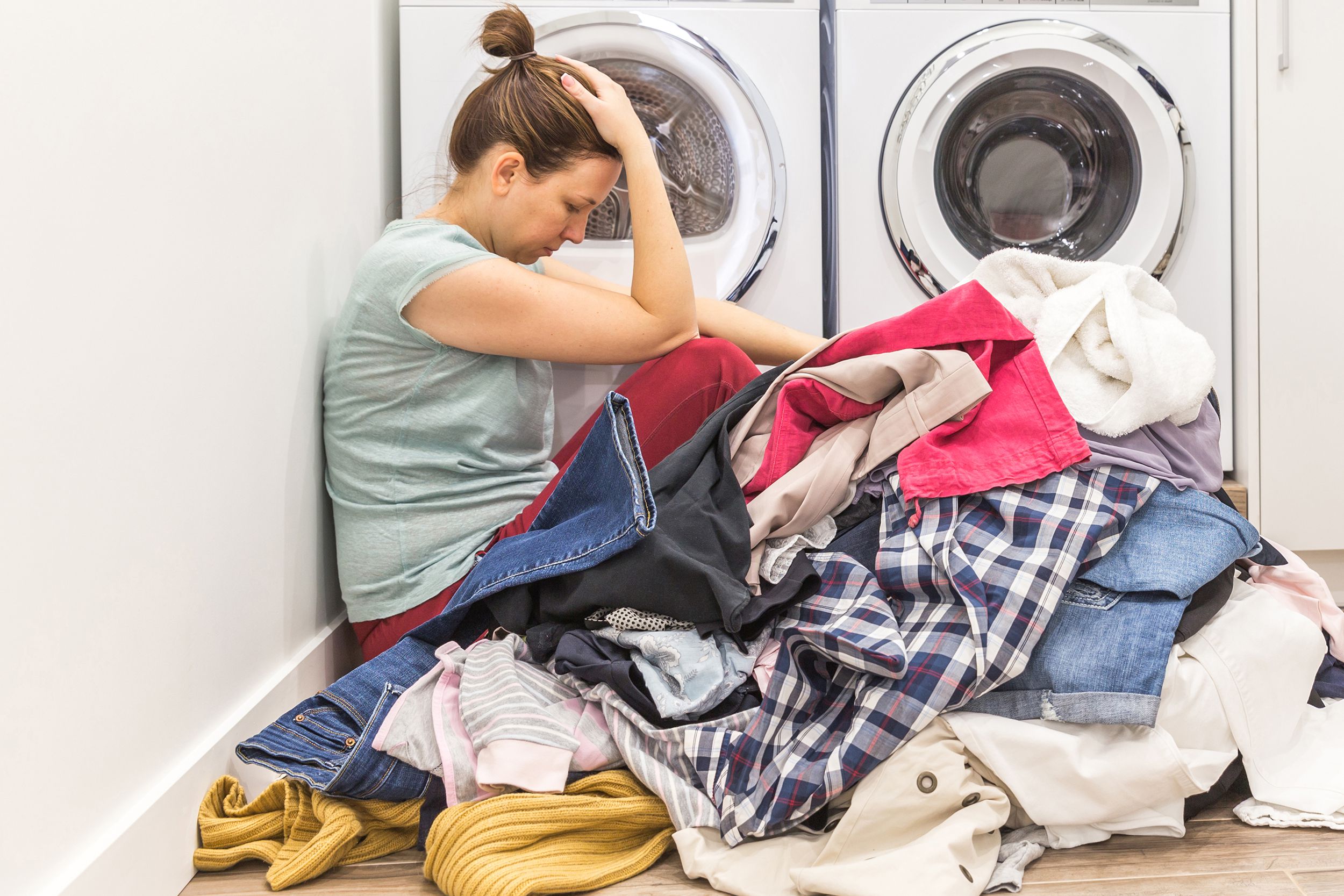 upset woman in laudry room sitting ona floor with dirty clothes, tired and frustrated
