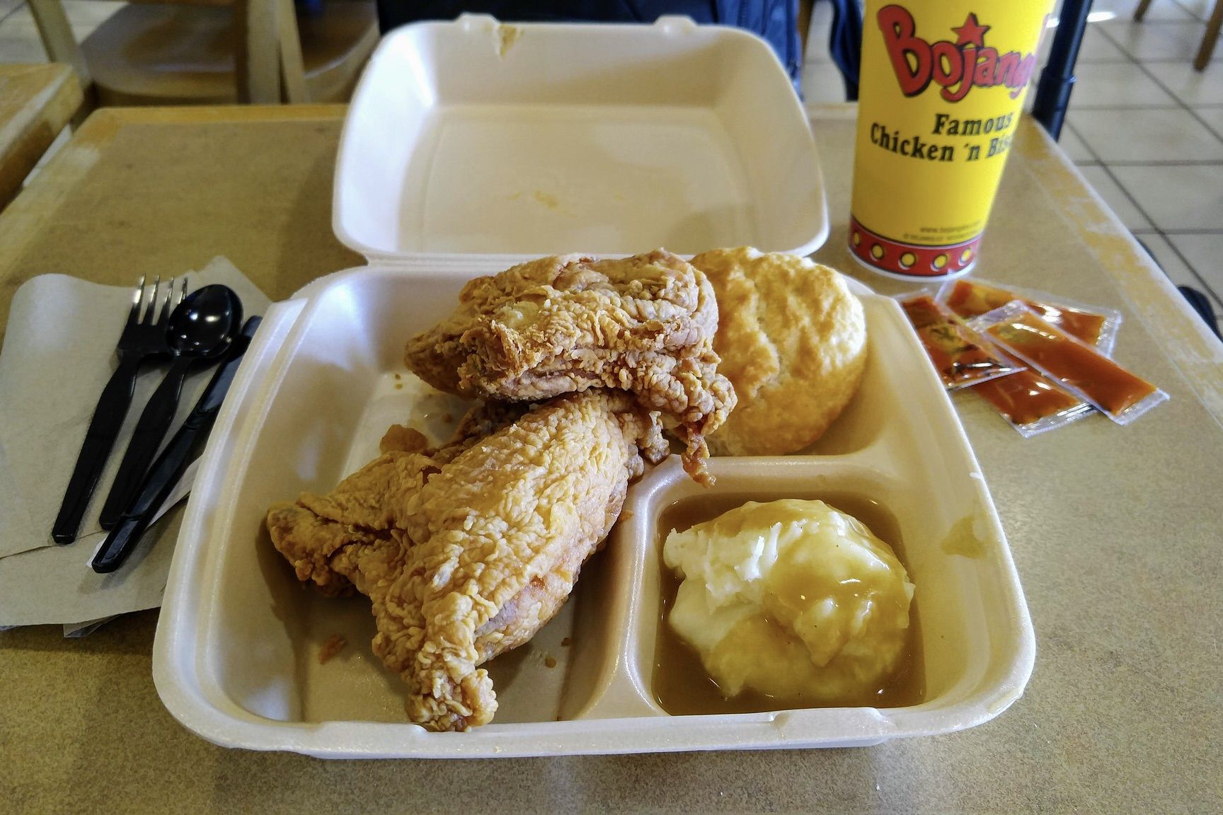 Fried chicken, biscuits and mashed potato with gravy in a styrofoam container on a plastic tray.