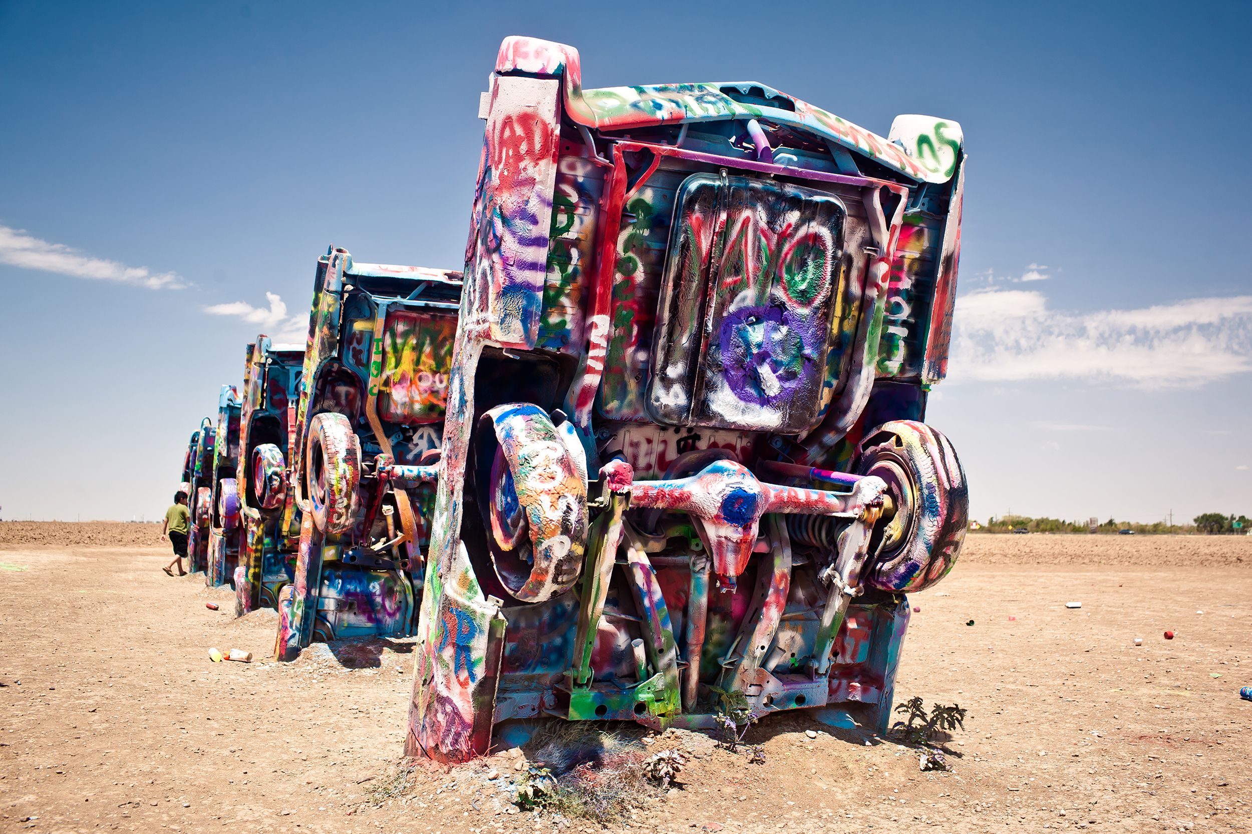 A row of colorful spray painted old Cadillacs in the dirt standing upright at Cadillac Ranch, Amarillo, Texas, a blue sky in the background on a sunny day