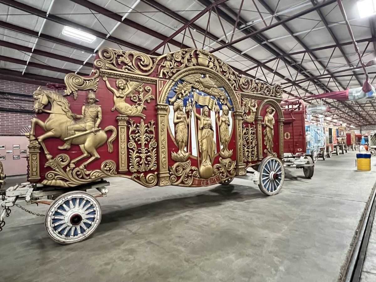 Red and gold circus carriage inside the Circus World Museum, Baraboo, Wisconsin, a row of other circus carriages going into the right background, on a concrete floor and warehouse ceiling