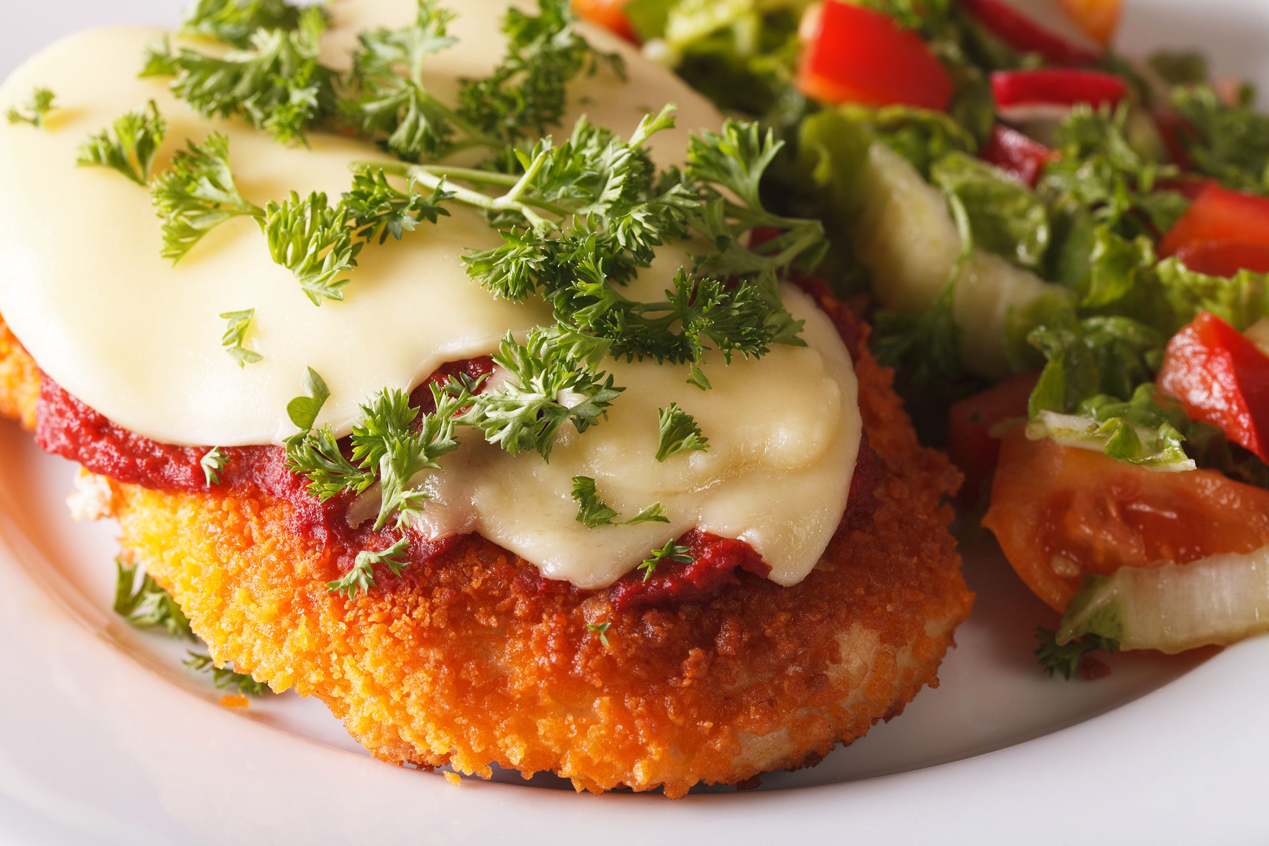 Closeup of chicken parmigiana on a white plate