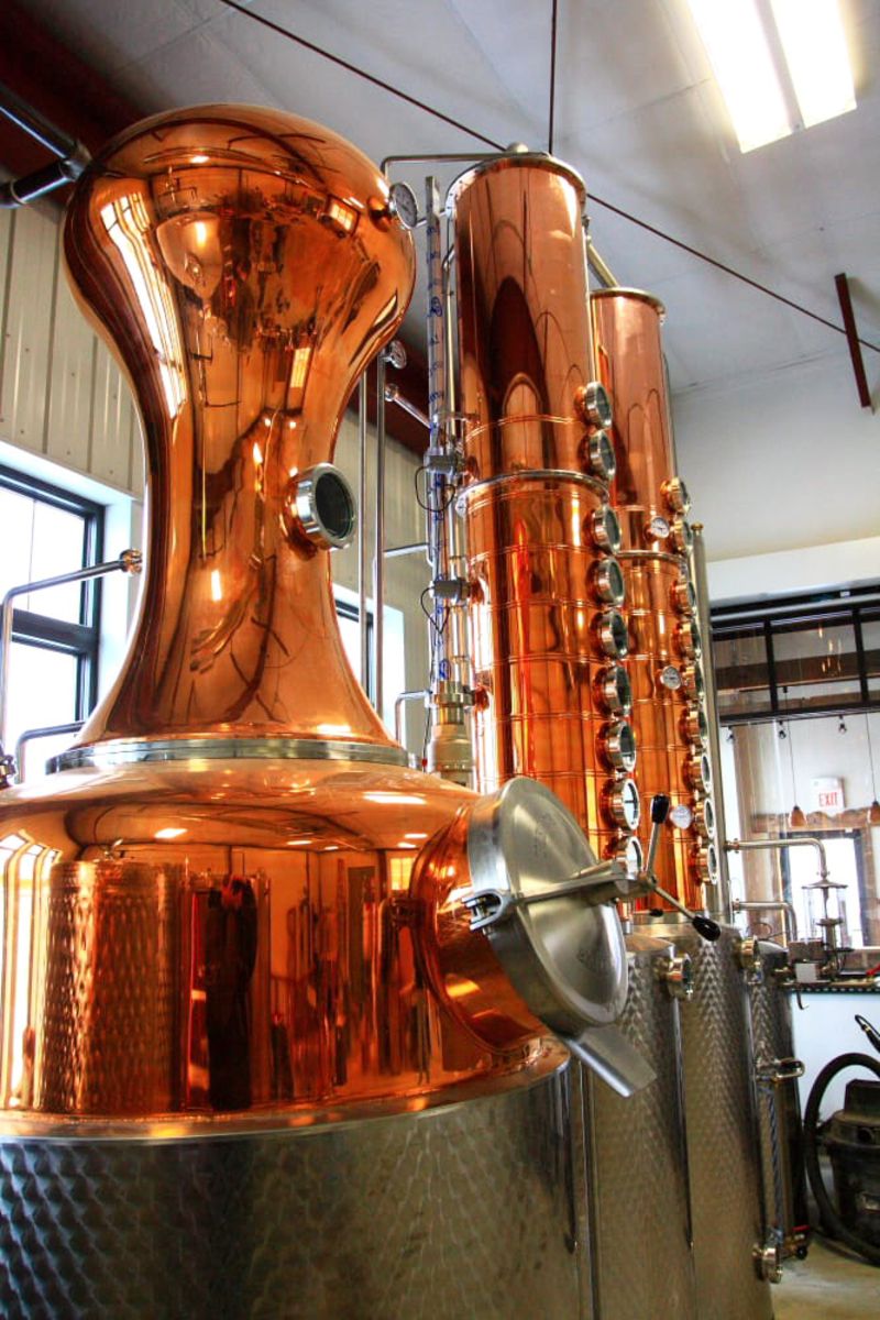 Line of copper brew kettles at Mississippi River Distilling Co., Le Claire, Iowa, beige wall and windows in the background