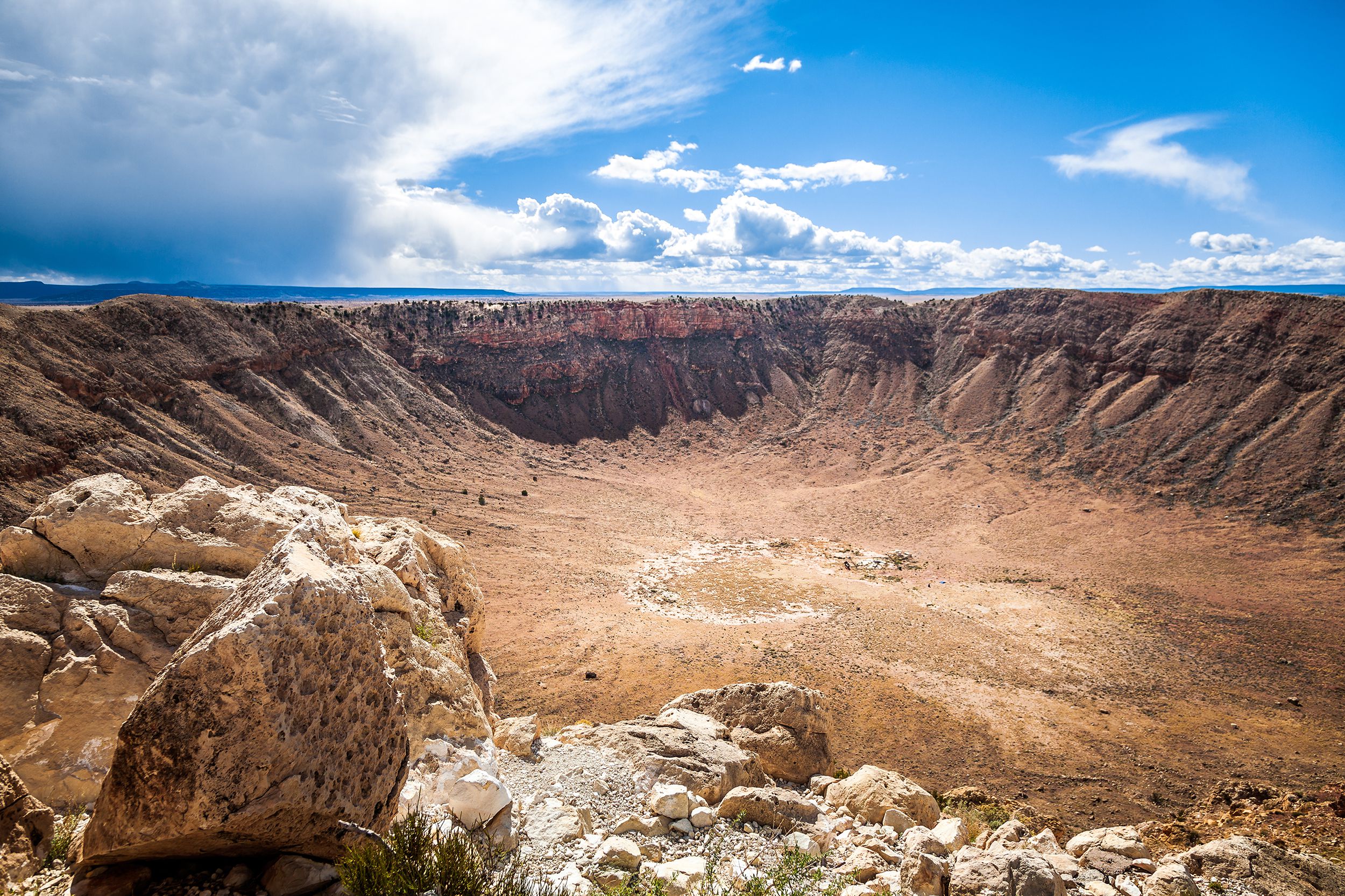 Expansive view of Meteor Crater near Winslow, Arizona, large rocks on the left foreground, on a sunny day with dramatic white clouds in a blue sky
