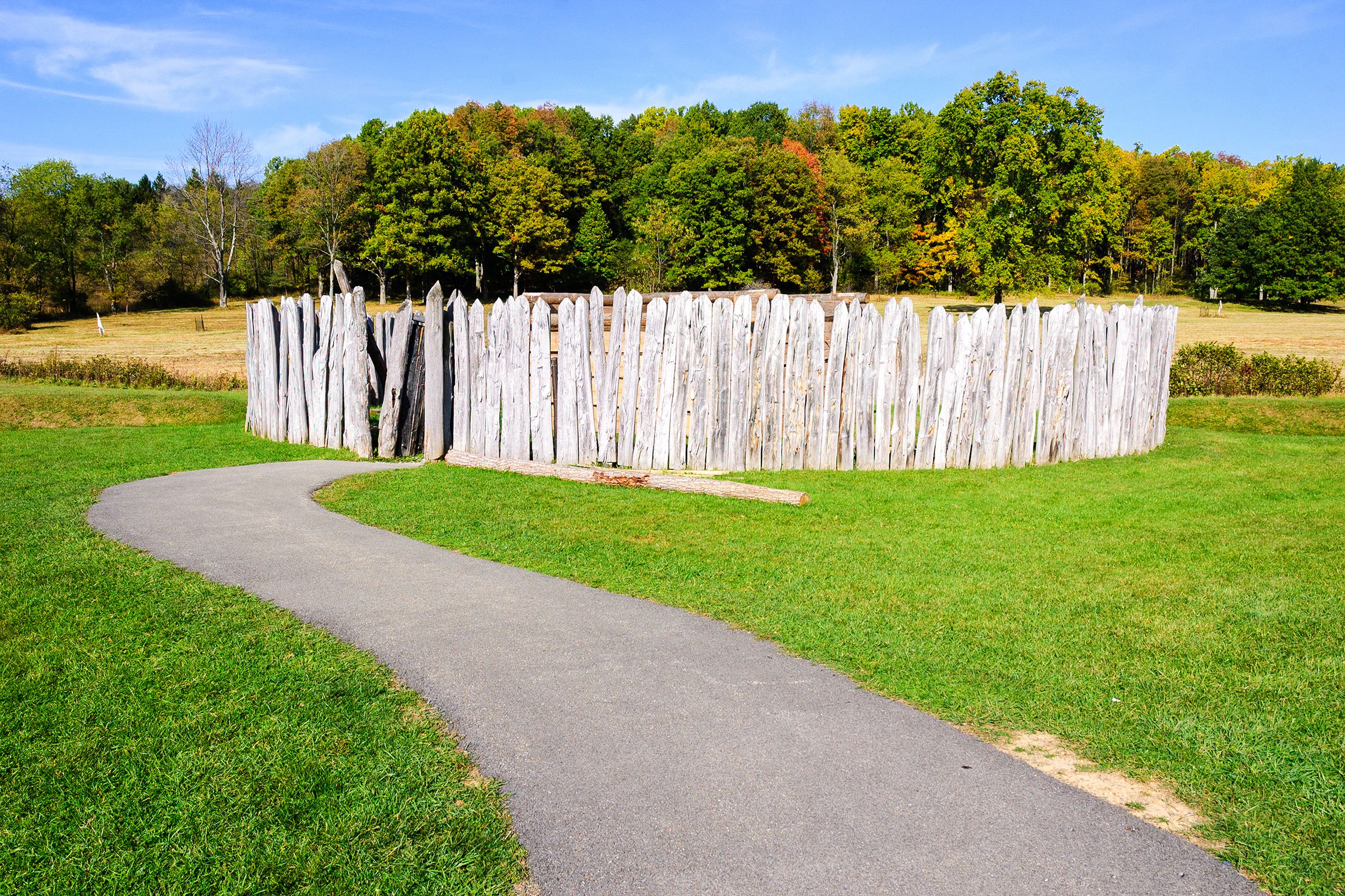 Fence wall of Fort Necessity National Battlefield, Farmington, Pennsylvania, walkway surrounded by green grass to fence wall, trees on hill during early autumn on a sunny day