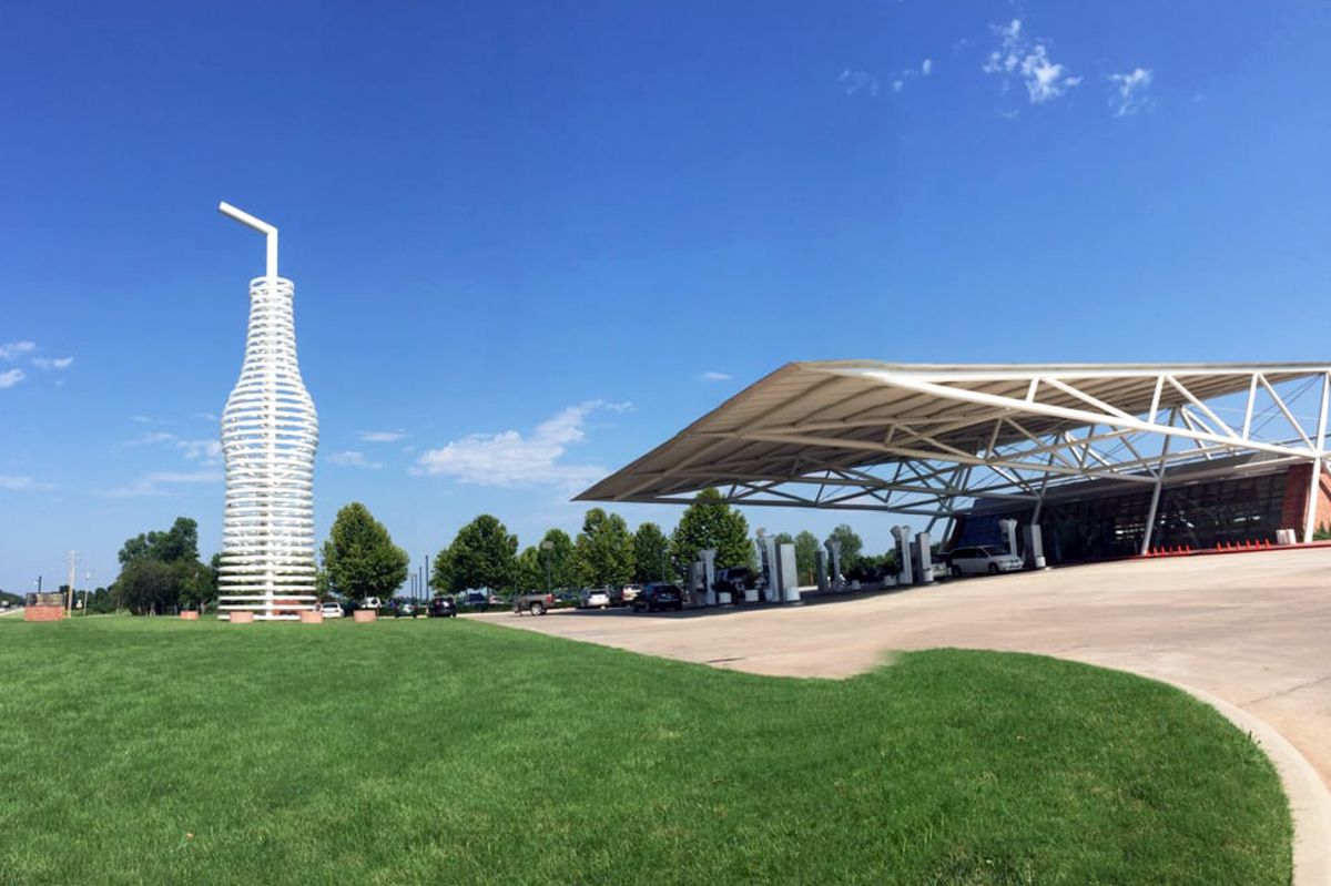 Front exterior of Pops Soda Ranch, Arcadia, Oklahoma, large white soda statue on the left and building on the right, on a slight hill, on a sunny day during summer
