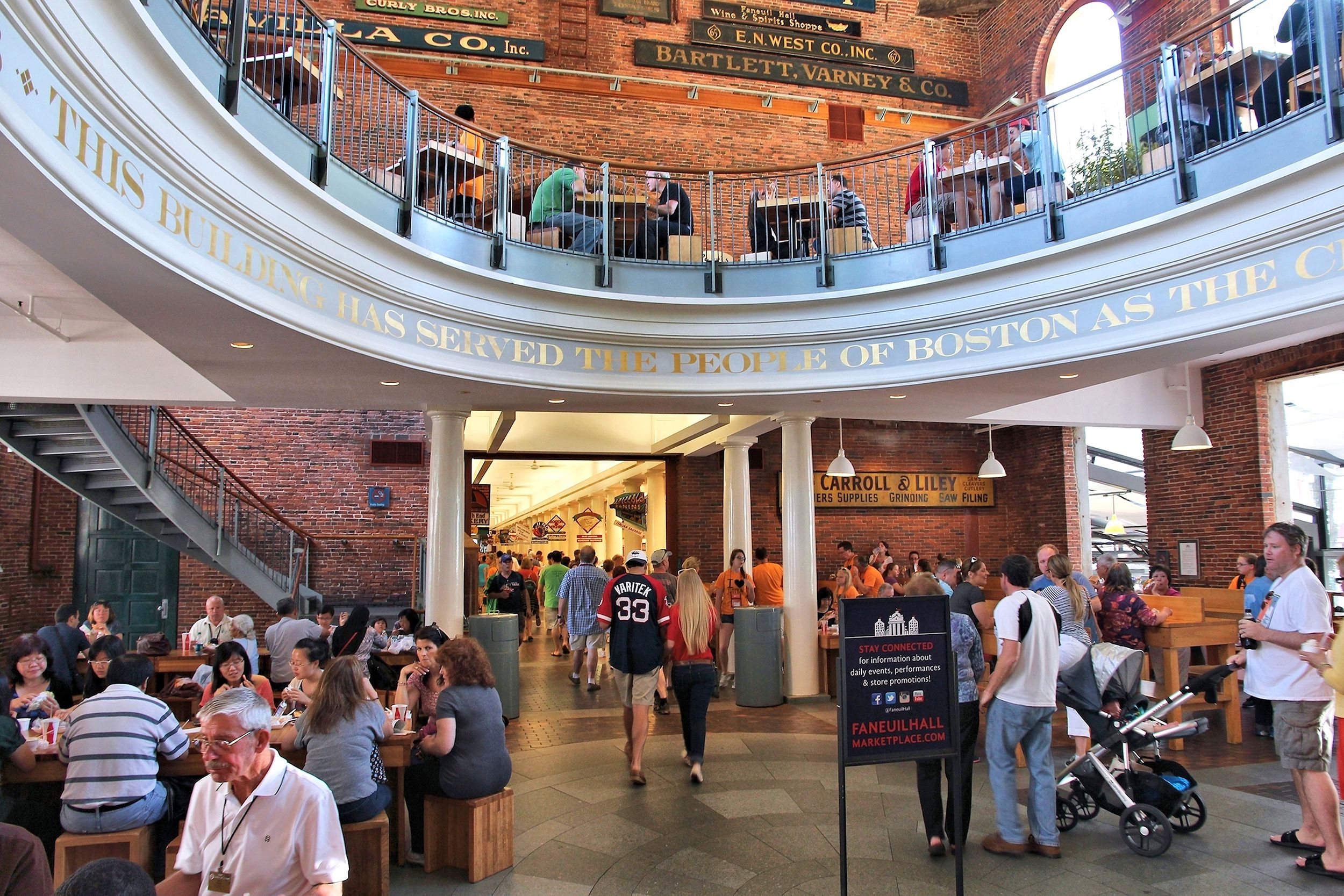 Lots of people walking and sitting down eating inside Faneuil Hall Marketplace, Boston, brick wall and a white second floor