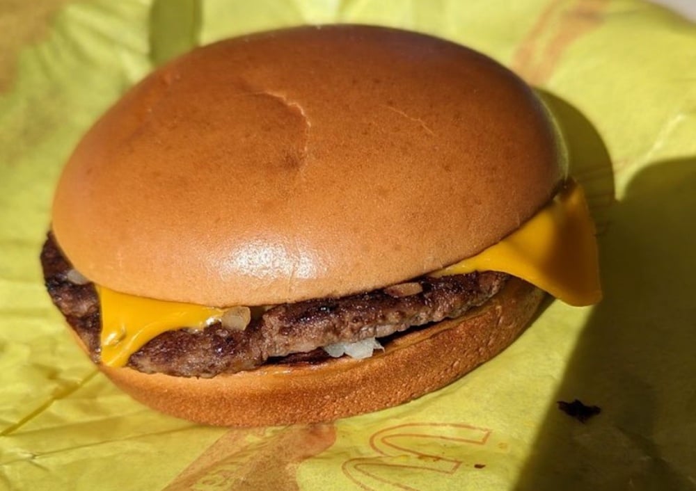 A cheeseburger on a yellow wrapper, featuring a beef patty with melted yellow cheese and chopped onions inside a soft, plain bun.