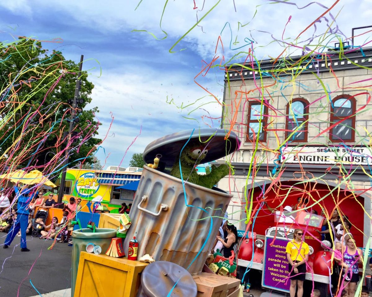 Oscar the Grouch at Sesame Place, Langhorne, Pennsylvania, Engine House on the right background and a food truck on the left, ribbon colorful confetti, on a bright sunny day during summer