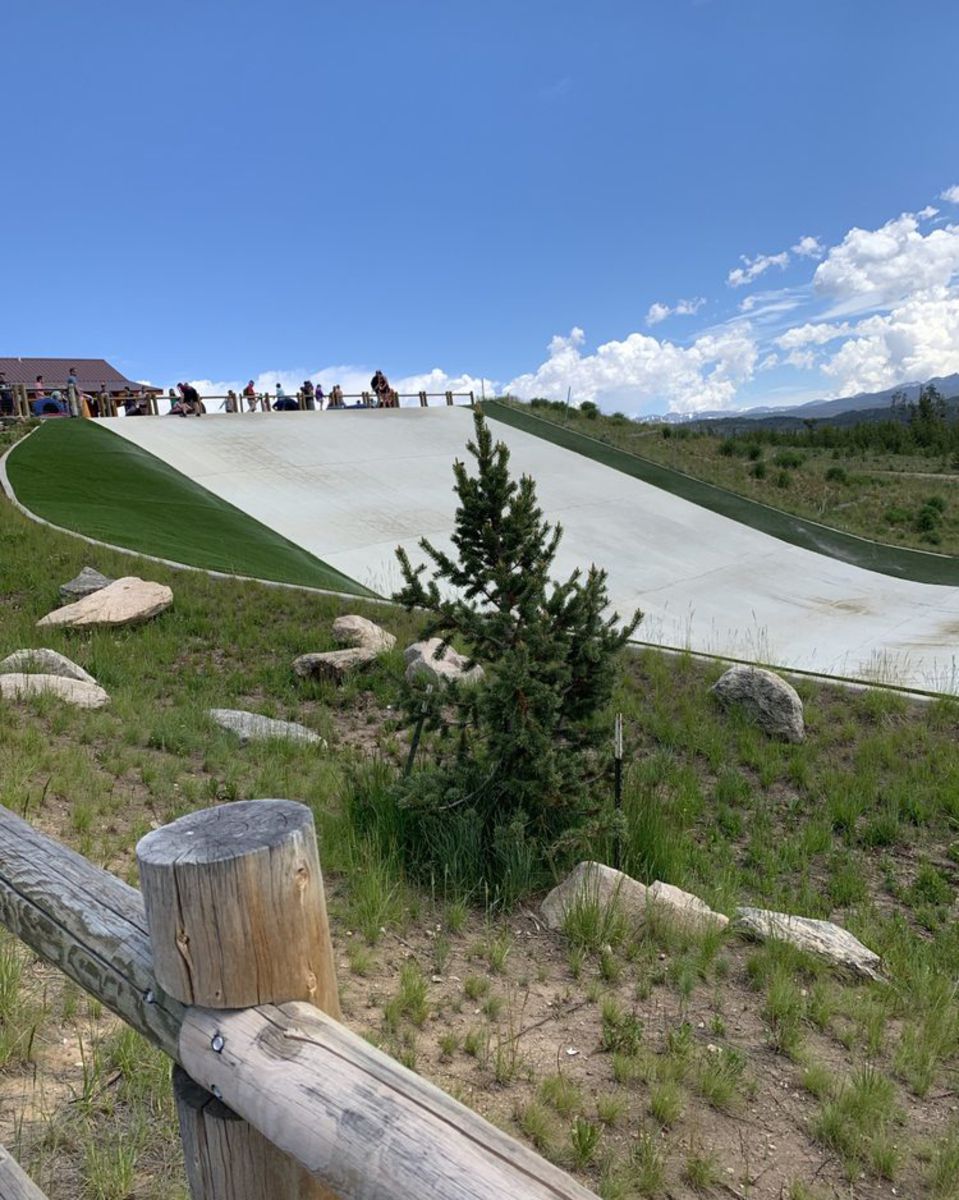 Snowflex Summer Slope, Snow Mountain Ranch, Granby, Colorado, people at the top about to slide down it, wooden fence in the foreground, on a sunny day