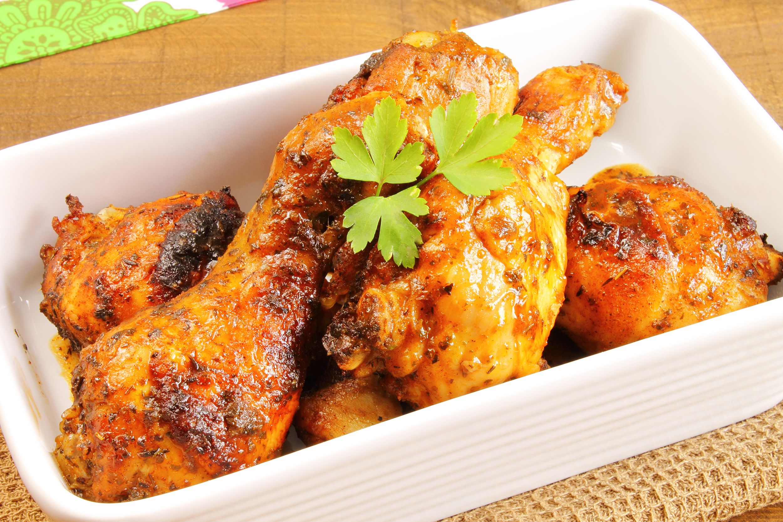 Closeup of spicy hot chicken legs in a rectangle white bowl on a natural napkin on a table