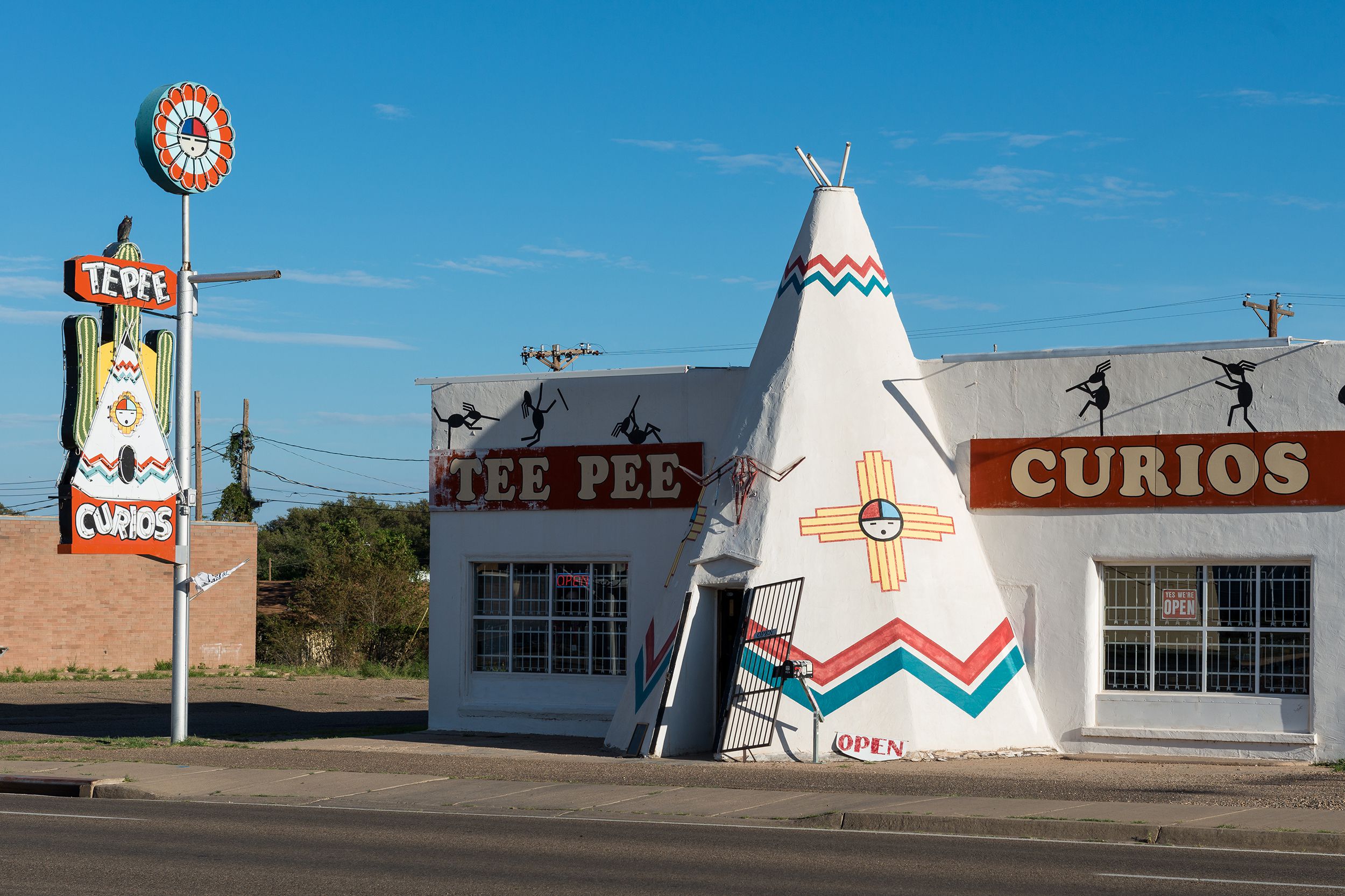 Tee Pee Curios, Tucumcari, New Mexico, white building with a tee pee for a door, opened front door, road in the foreground on a sunny day day