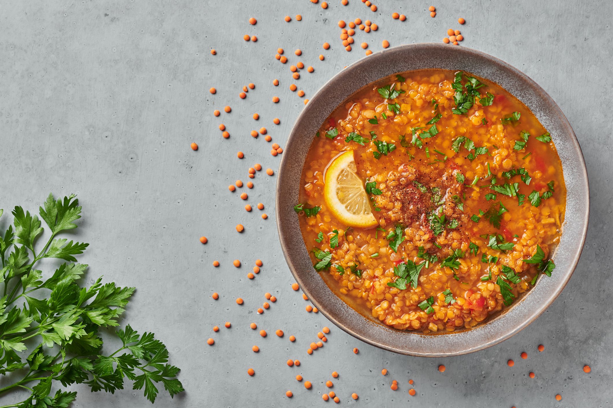 Red lentils tomato soup with parsley and lemon in gray plate on concrete table top. Vegetarian dish. Copy space